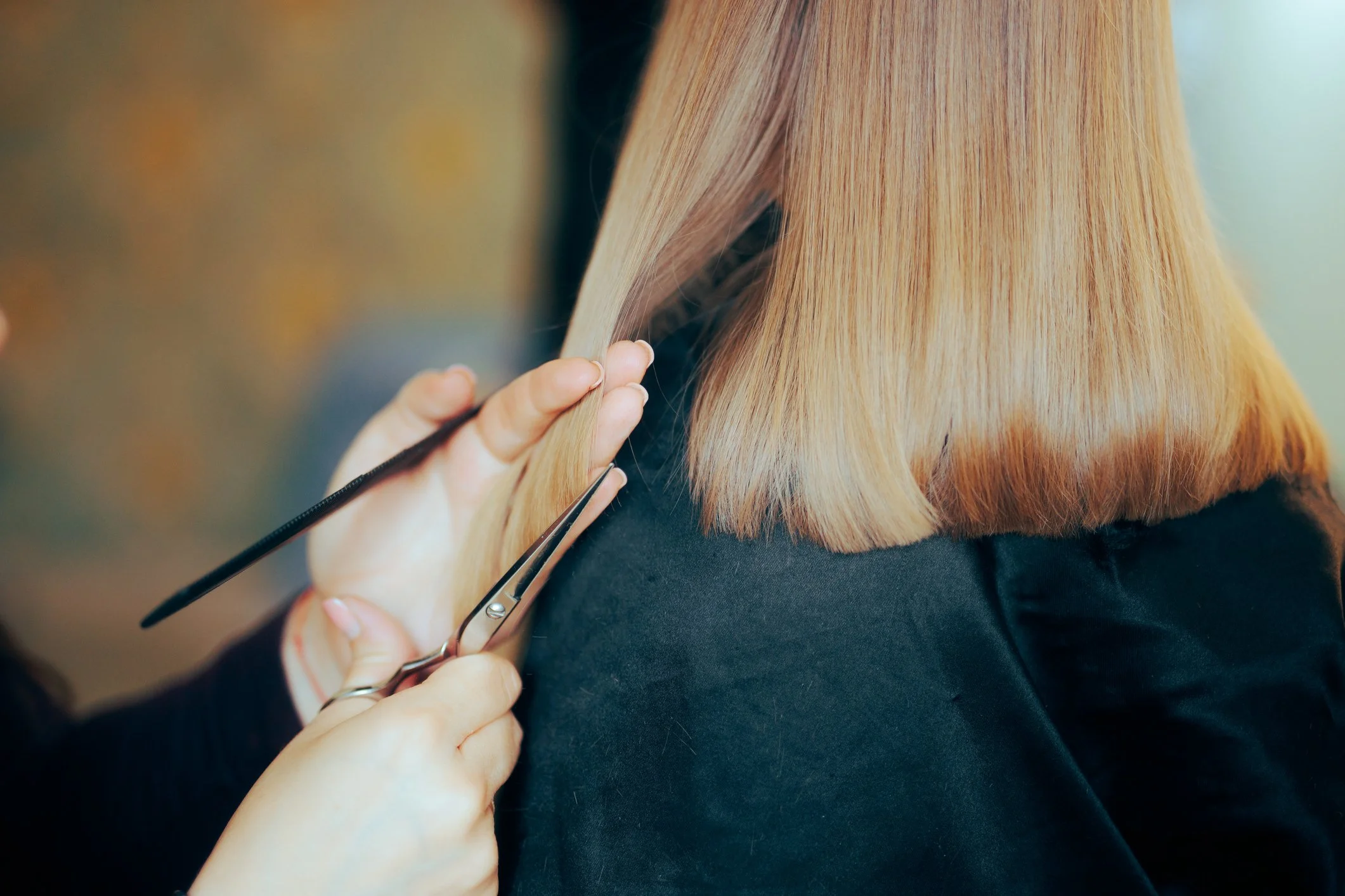 Close-up of a hairdresser cutting a woman's blonde hair with scissors in a salon.