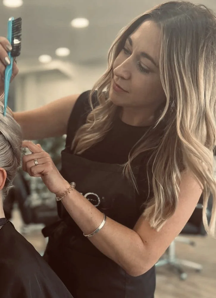 A hairstylist is coloring a client's hair with foil. The stylist has long wavy hair and is focused on her work in a salon.
