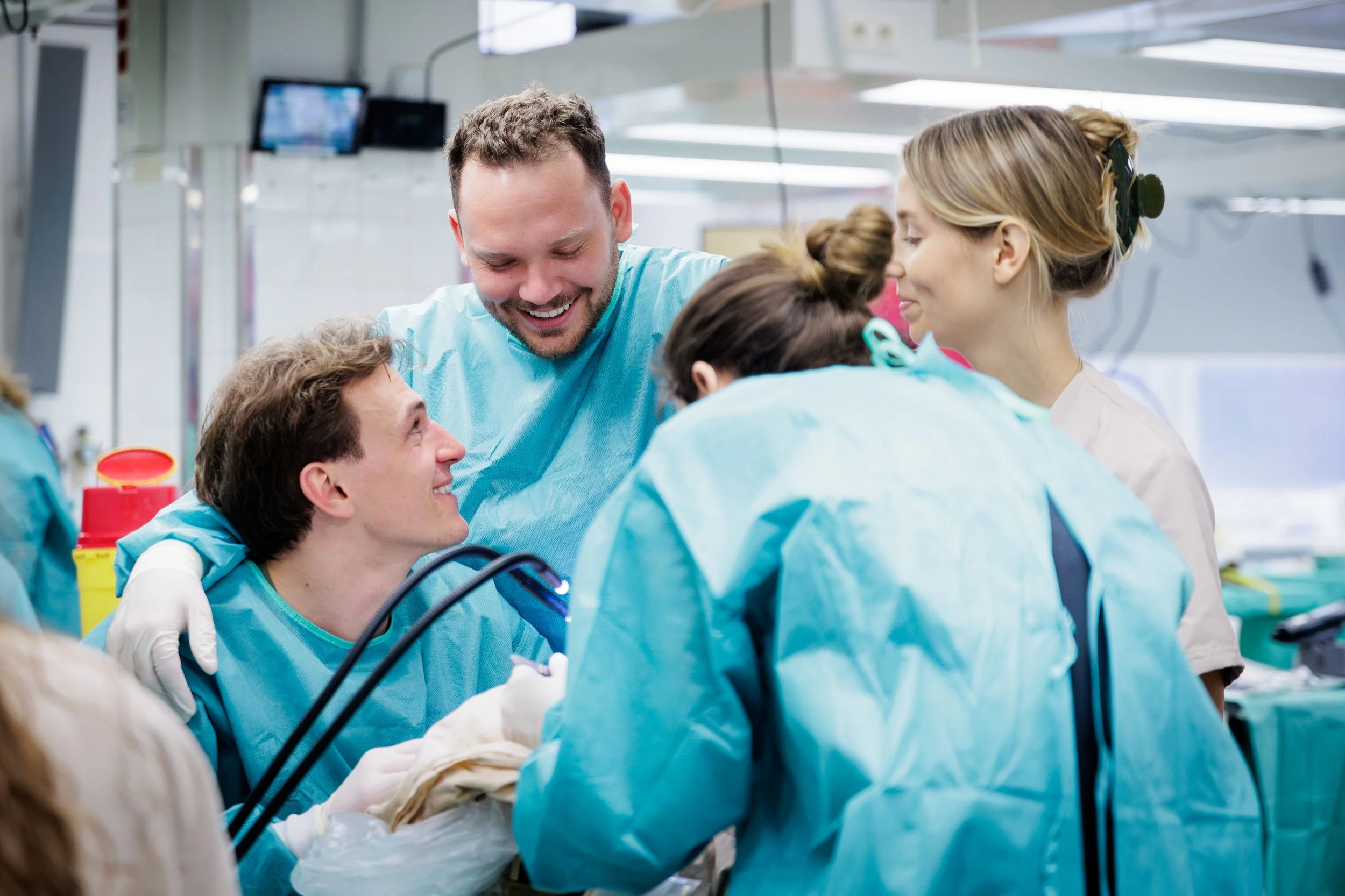 A group of medical professionals, including a male doctor and a female nurse, smiling and gathering around an attentive male patient during a medical procedure in a hospital operating room.