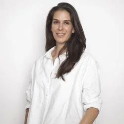 A woman with long dark hair wearing a white shirt, smiling at the camera.