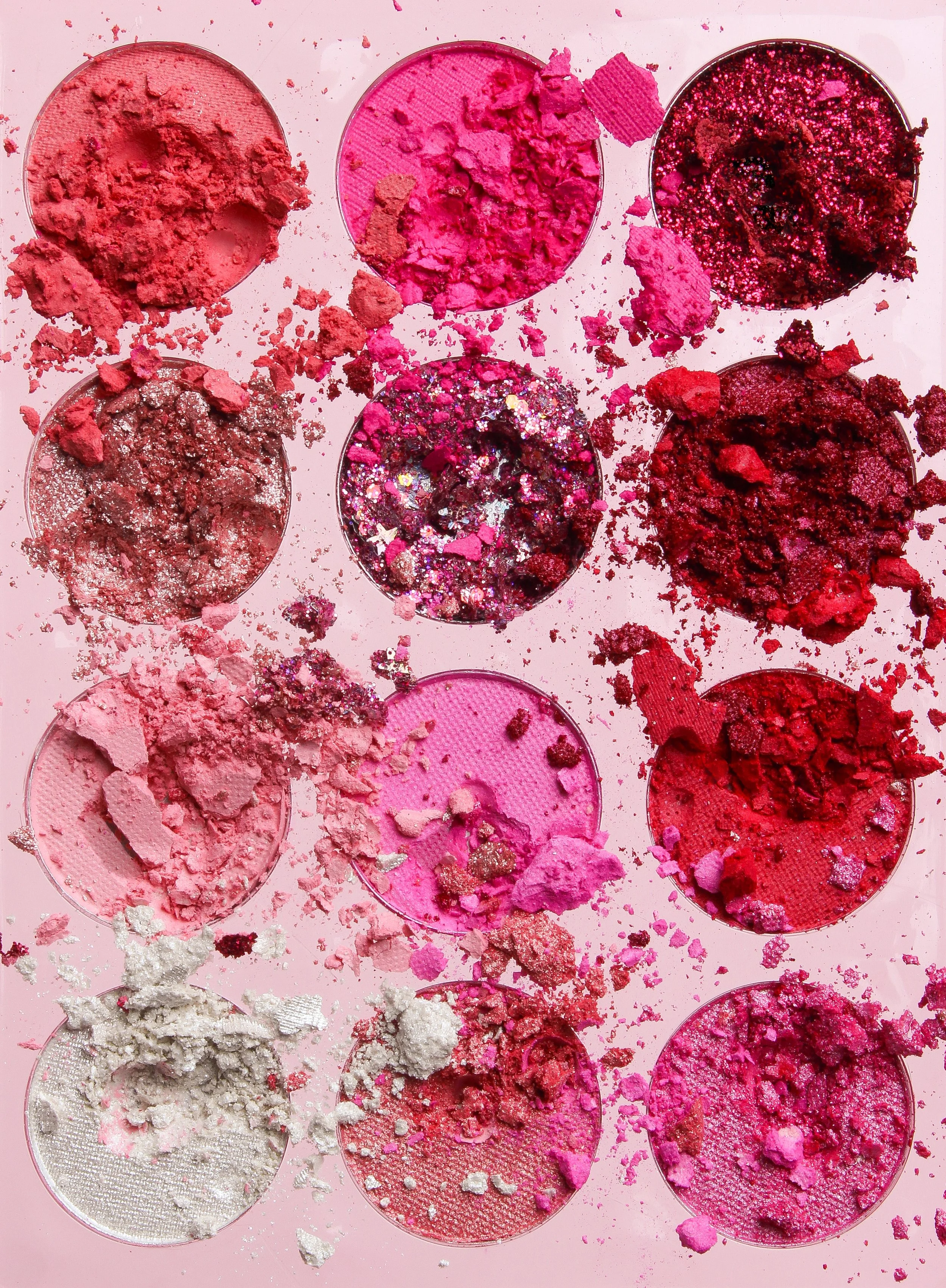 A pink eyeshadow palette with many spilled and crushed powders in shades of pink, red, and silver.
