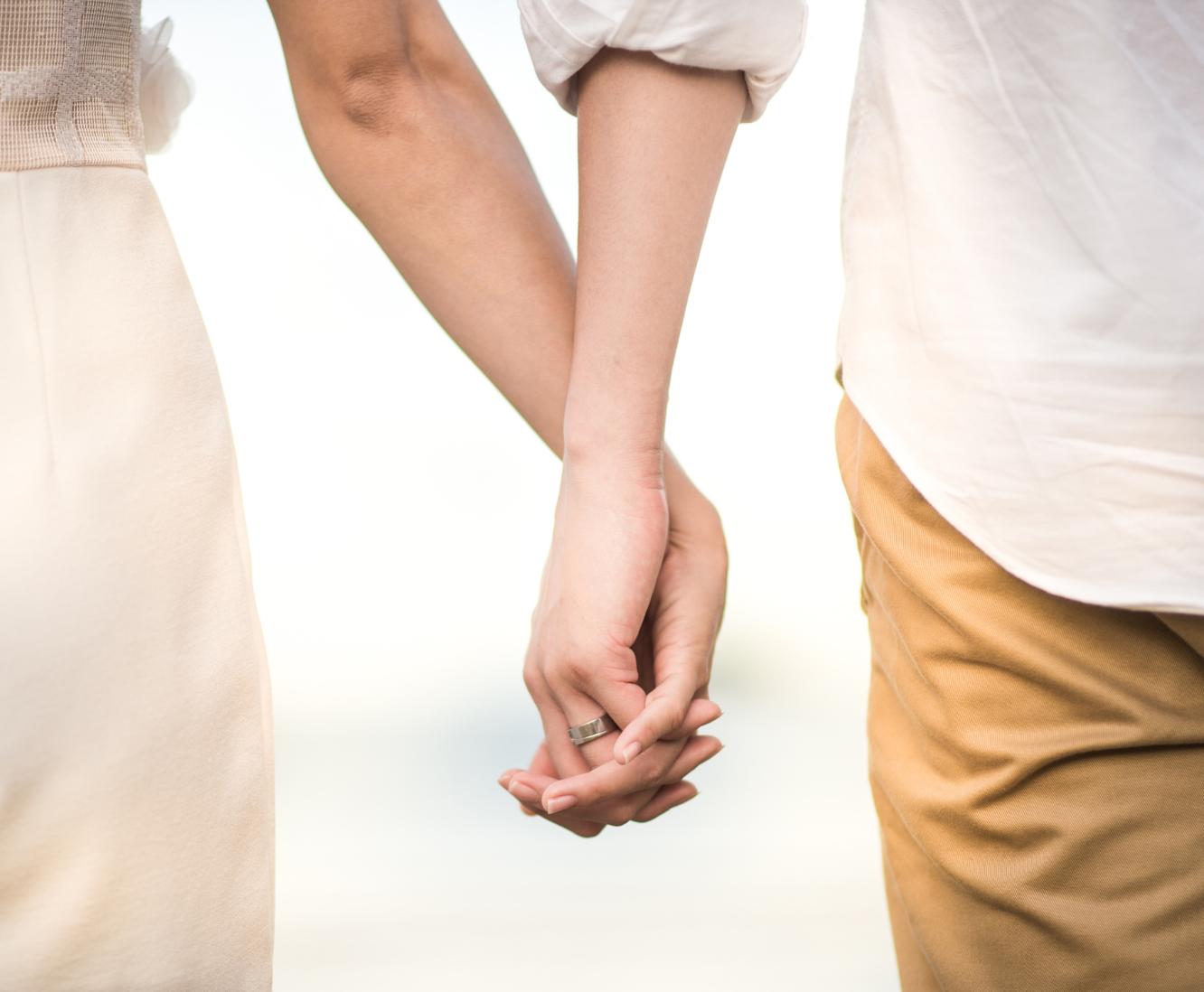 A close-up of a couple holding hands, showing the woman's hand with a wedding ring and the man's hand from the side.