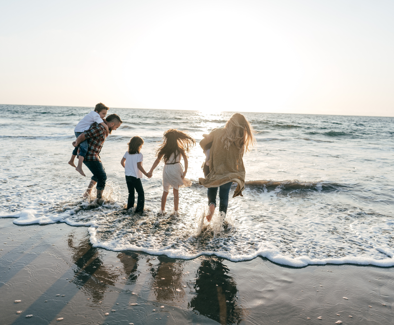 Family with children playing in the ocean waves at sunset on the beach.