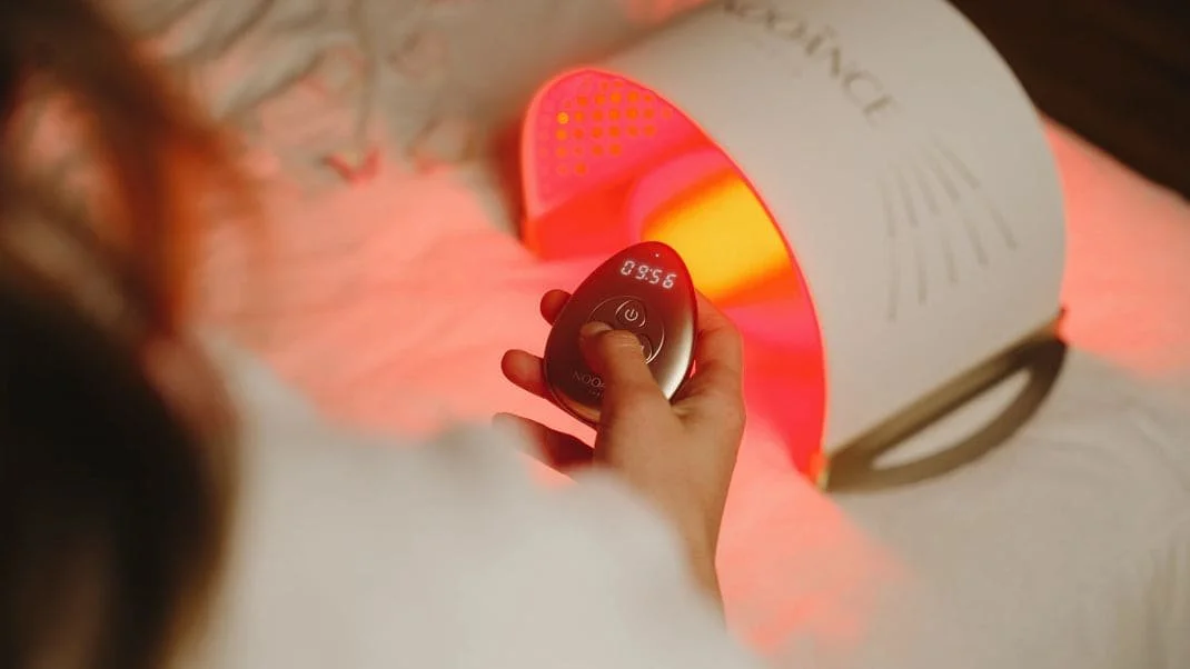 Une personne utilise une lampe de luminothérapie avec un contrôle à distance. La lampe émet une lumière rouge/orange