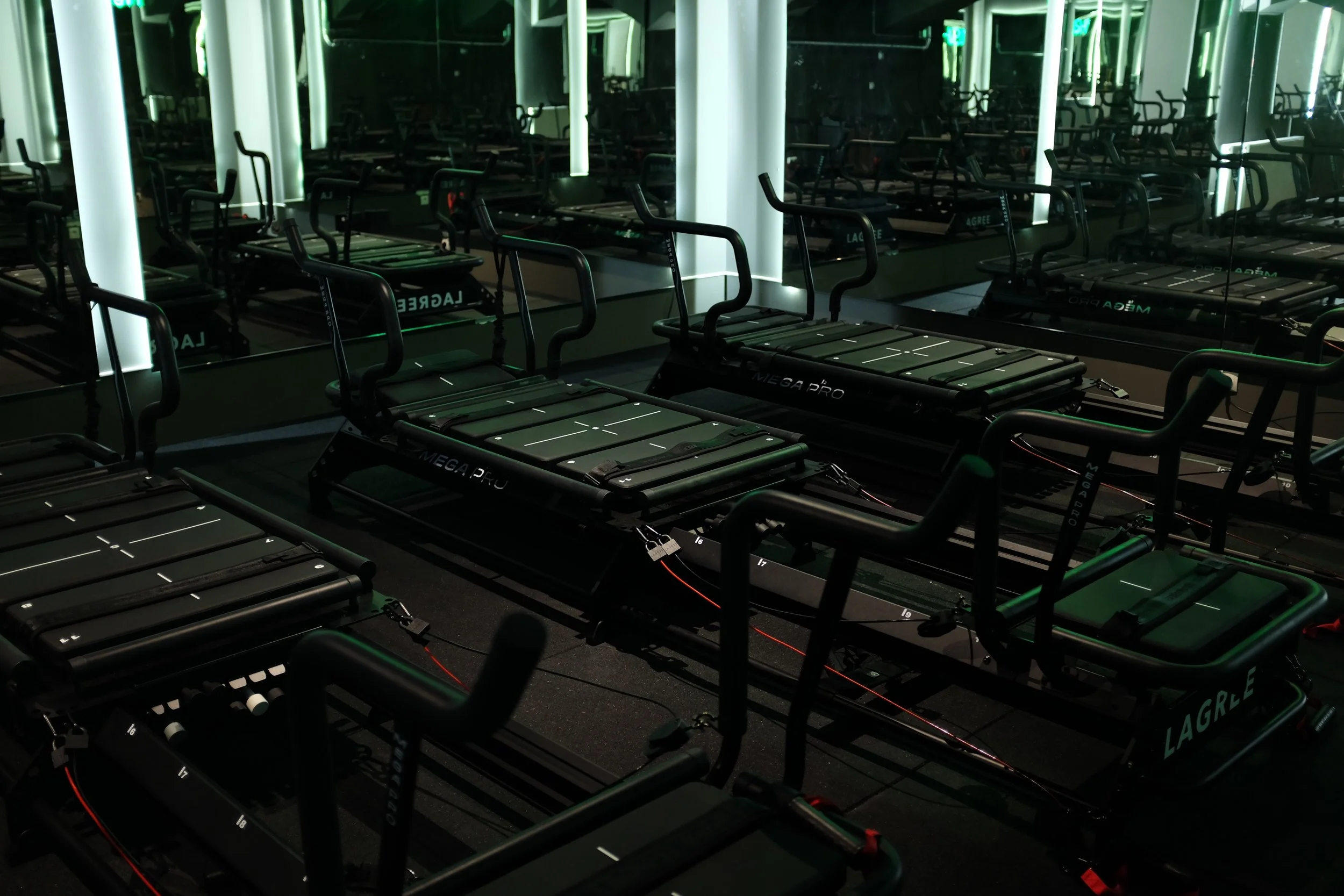 Multiple black Lagree Megaformer in a Lagree gym in Vienna with mirrors on the wall reflecting green lighting.