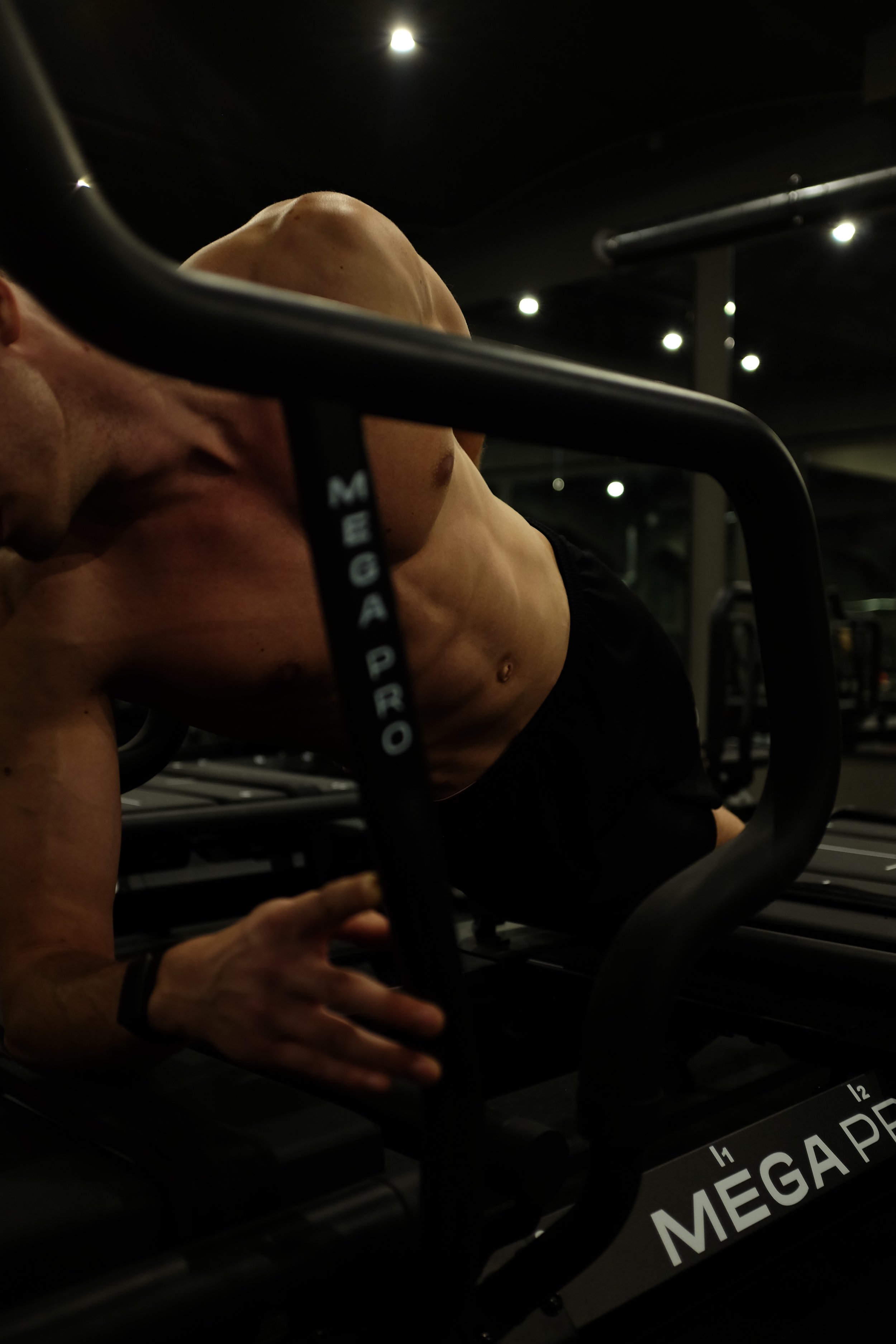 A shirtless man exercising on a Lagree fitness Megaformer at a gym, with a focus on his muscular torso.