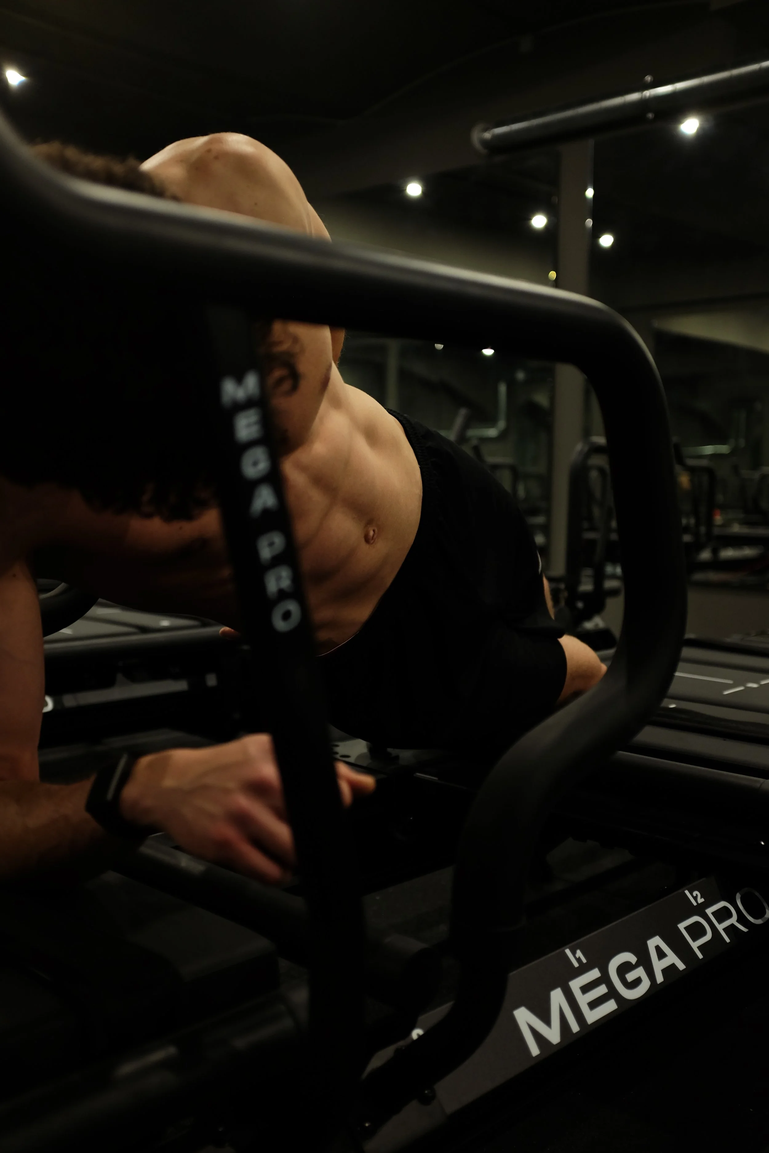 Person doing a plank exercise on a fitness Lagree machine in a gym, with focus on their muscular torso and abs.