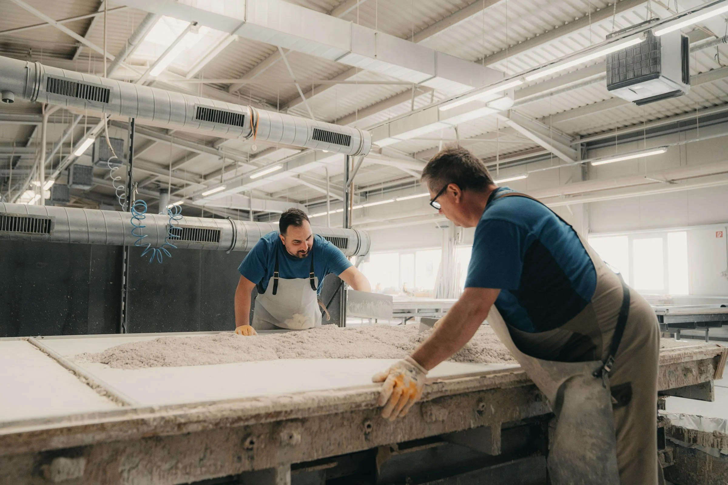 Zwei Personen giessen den Sand in die Gussform für ein Mineralit-Element