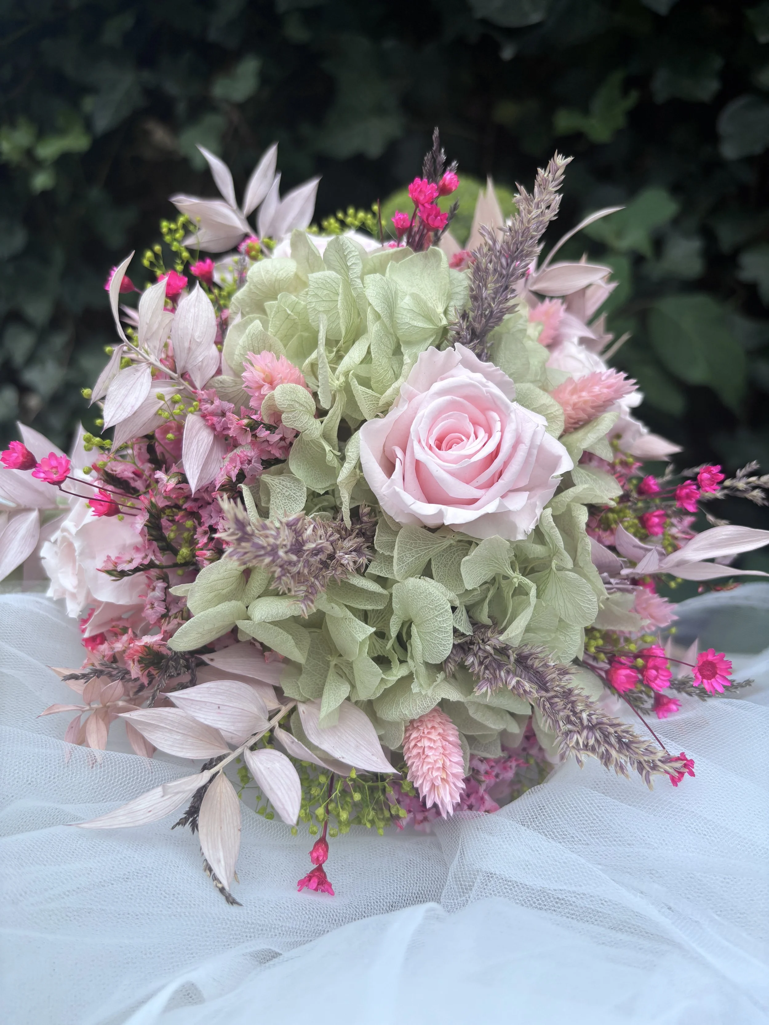 Bouquet de mariée en fleurs séchées et stabilisées aux tons rose poudré, vert sauge et beige naturel, réalisé à la main par L’Atelier Fleurs & Sens près de Valenciennes. Cette création florale bohème et romantique associe hortensia stabilisé, roses s