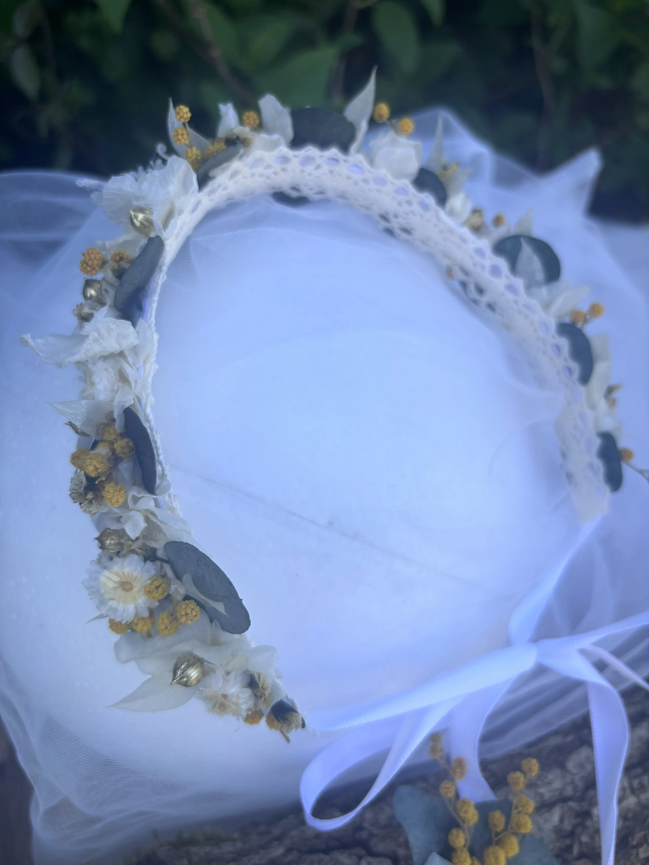 Couronne de fleurs blanches, jaunes et vertes sur un tissu blanc.