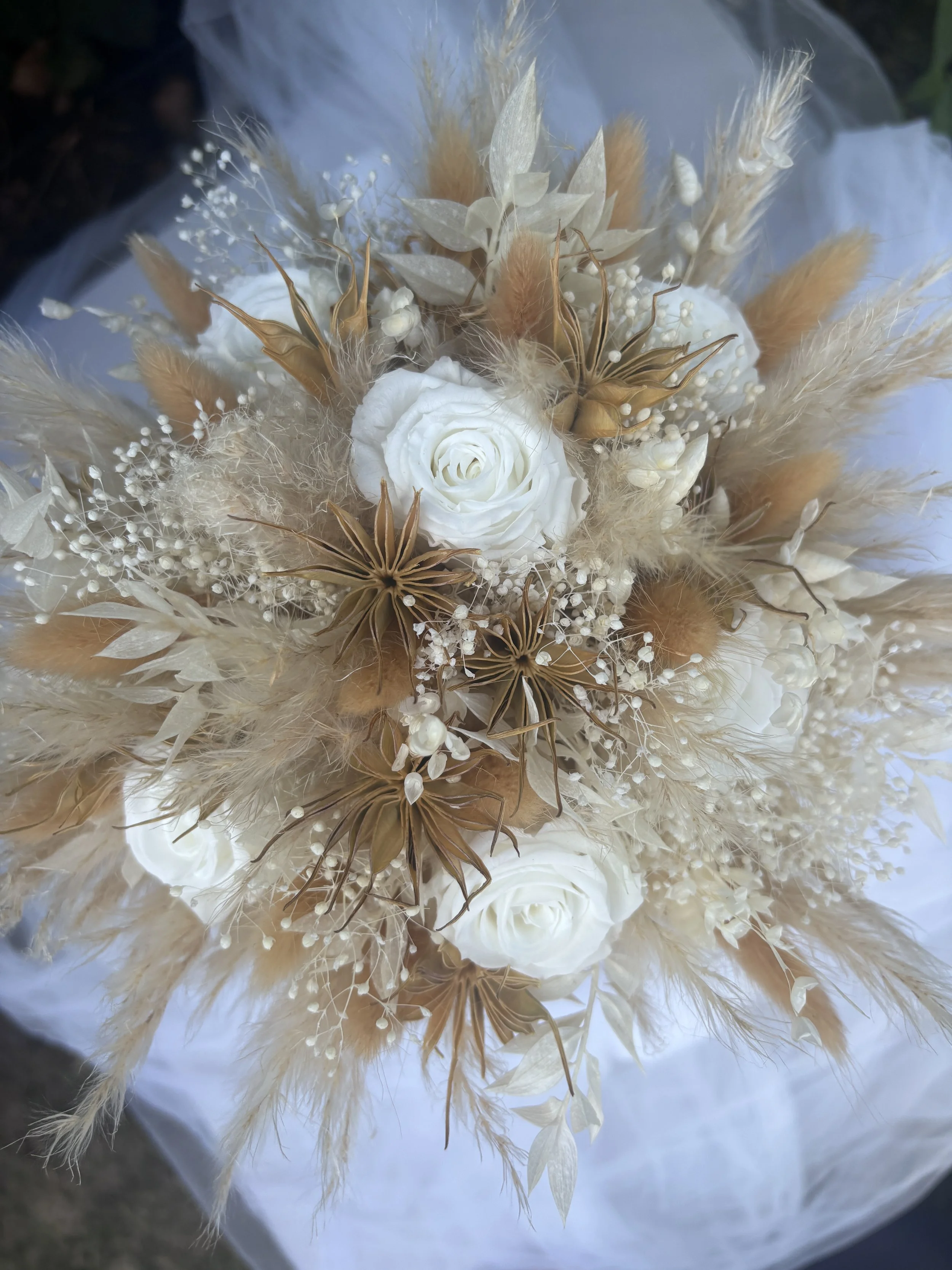 Bouquet de mariée réalisé artisanalement en fleurs séchées et stabilisées. Une création romantique et aérienne mêlant roses blanches, gypsophile, pampas et feuillages naturels dans des nuances ivoire, nude et rose poudré. Création sur mesure par L’At