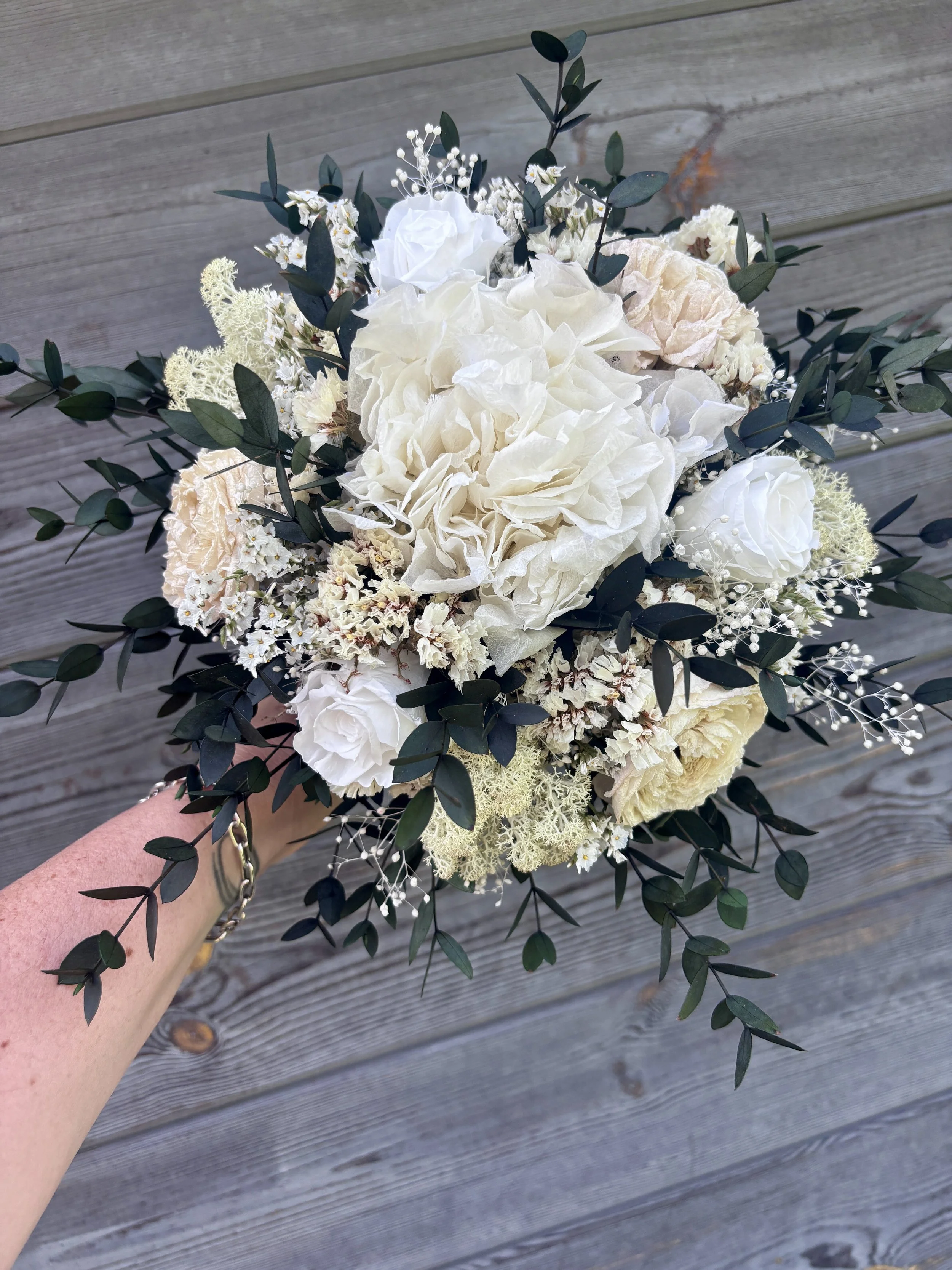 Bouquet de mariée bohème chic en fleurs séchées et stabilisées, composé de pivoines blanches, roses stabilisées, statice blanc, mousse végétale et feuillage d’eucalyptus noir. Cette création artisanale associe élégance, douceur et caractère pour un m