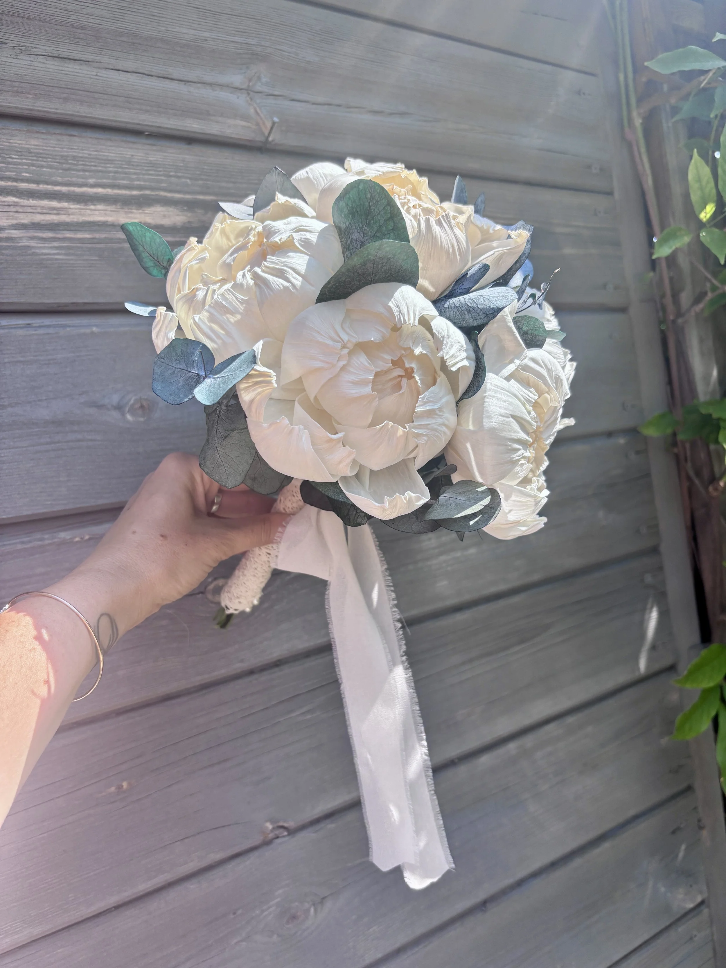 Bouquet de mariée élégant et intemporel composé de grandes pivoines ivoire en bois de Sola, associées à un feuillage d’eucalyptus. Une création florale durable, réalisée artisanalement et personnalisable selon les couleurs du mariage par L’Atelier Fl