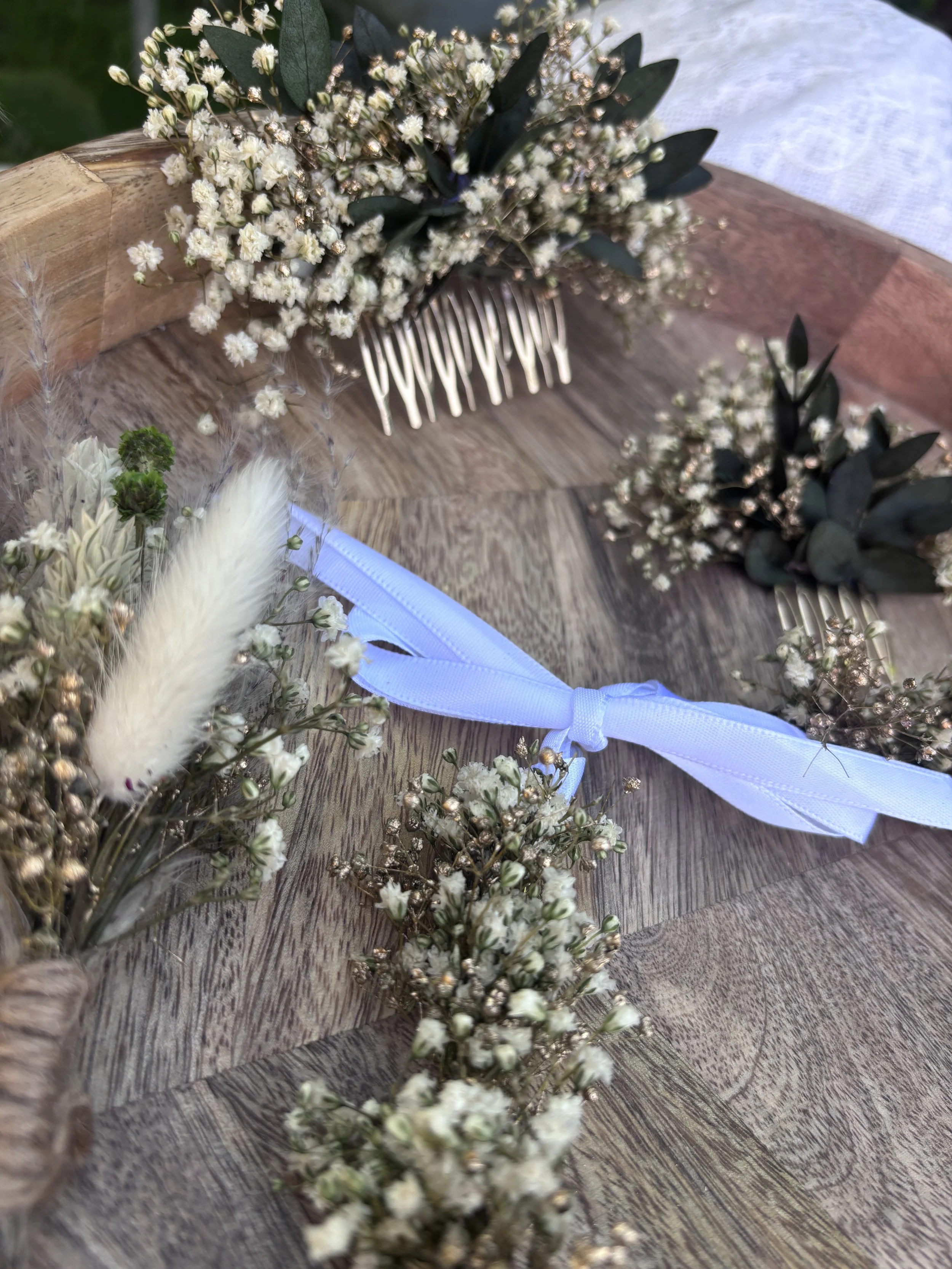 Un bouquet de fleurs blanches avec des feuilles vertes, attaché avec un ruban blanc, placé sur une surface en bois.