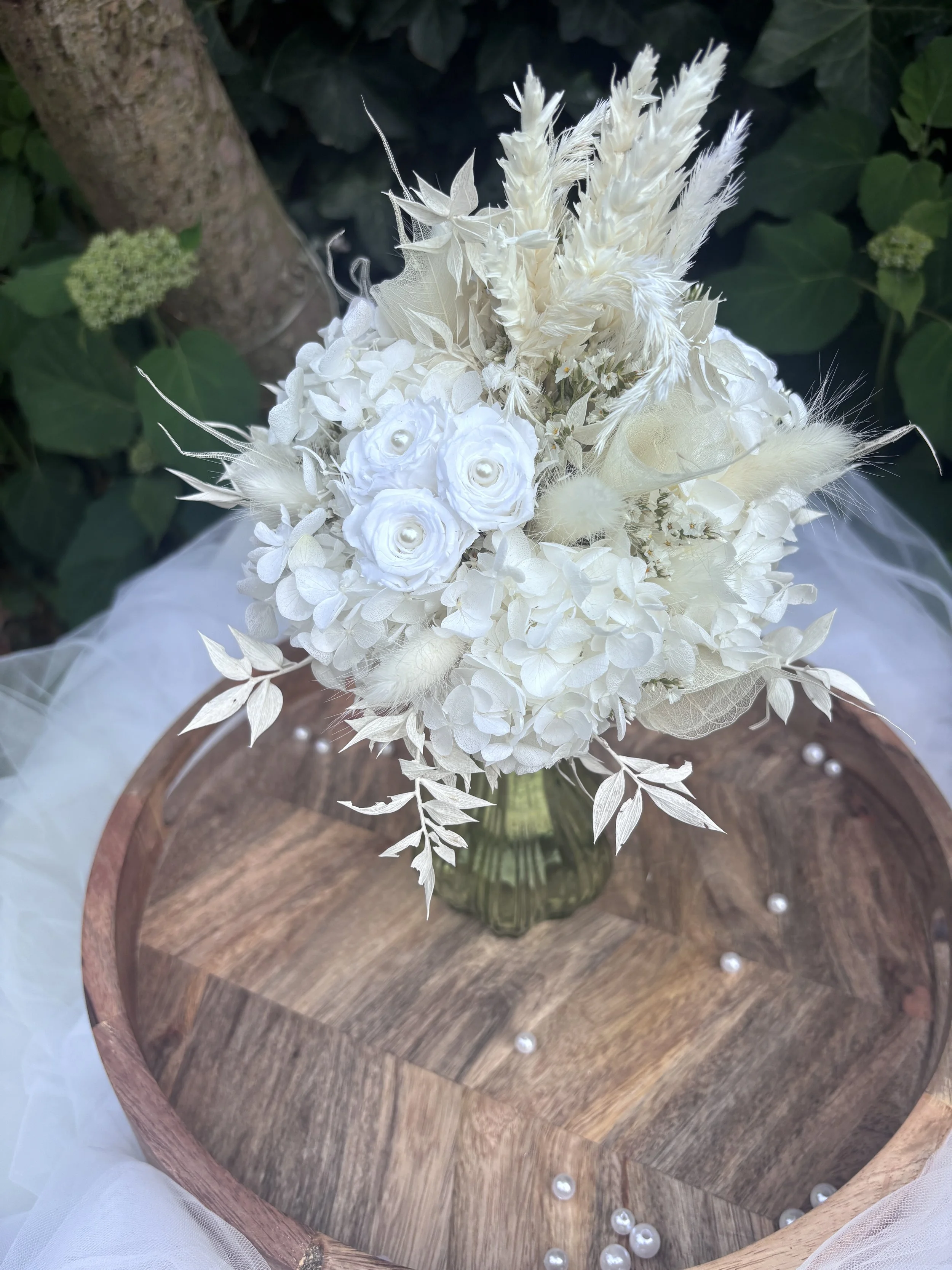 Bouquet de mariée en fleurs séchées et stabilisées blanches, réalisé artisanalement dans un esprit bohème chic et romantique. Cette création florale associe hortensias stabilisés, roses éternelles ornées de perles, arums délicats, feuillages blanchis