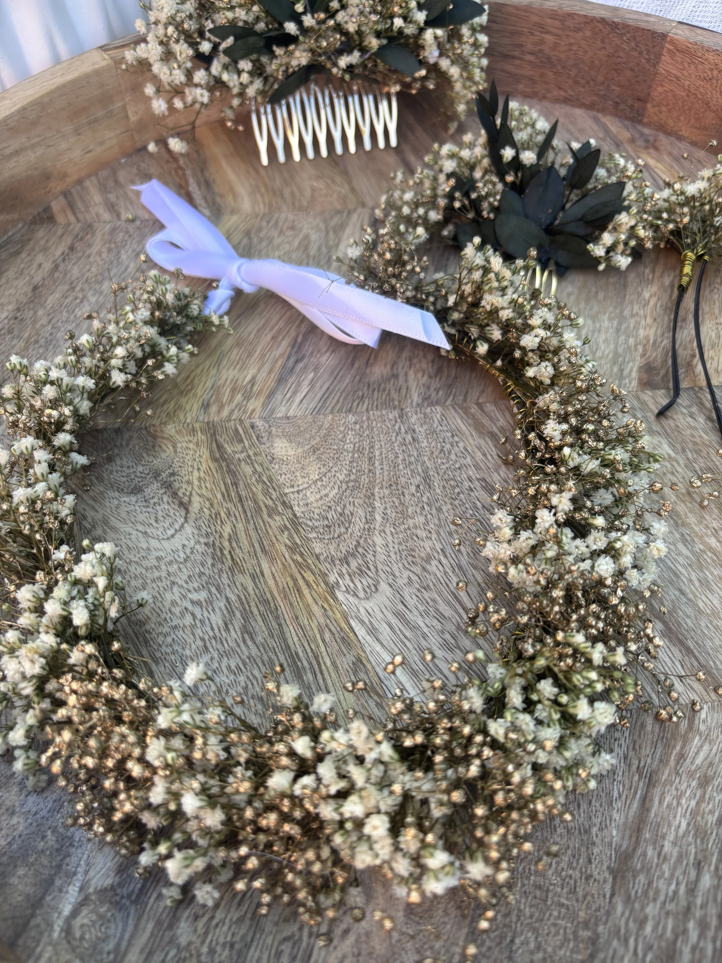 Couronne de fleurs blanches et feuillage vert disposée sur une table en bois.