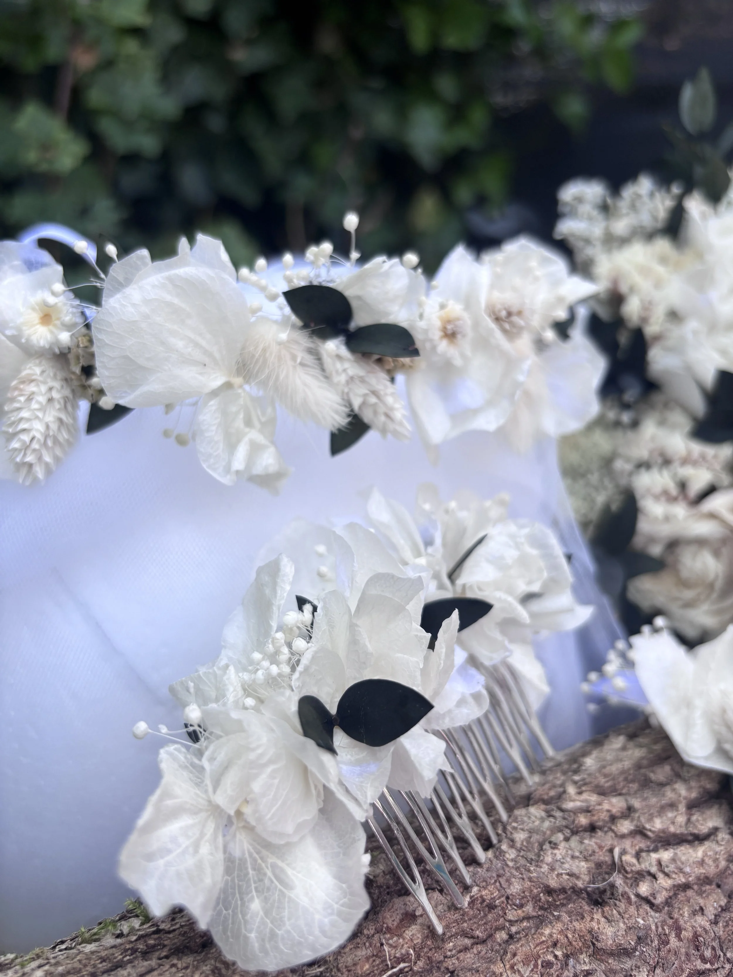 Une décoration florale blanche avec des fleurs en tissu et des feuilles noires, fixée sur une branche d'arbre.