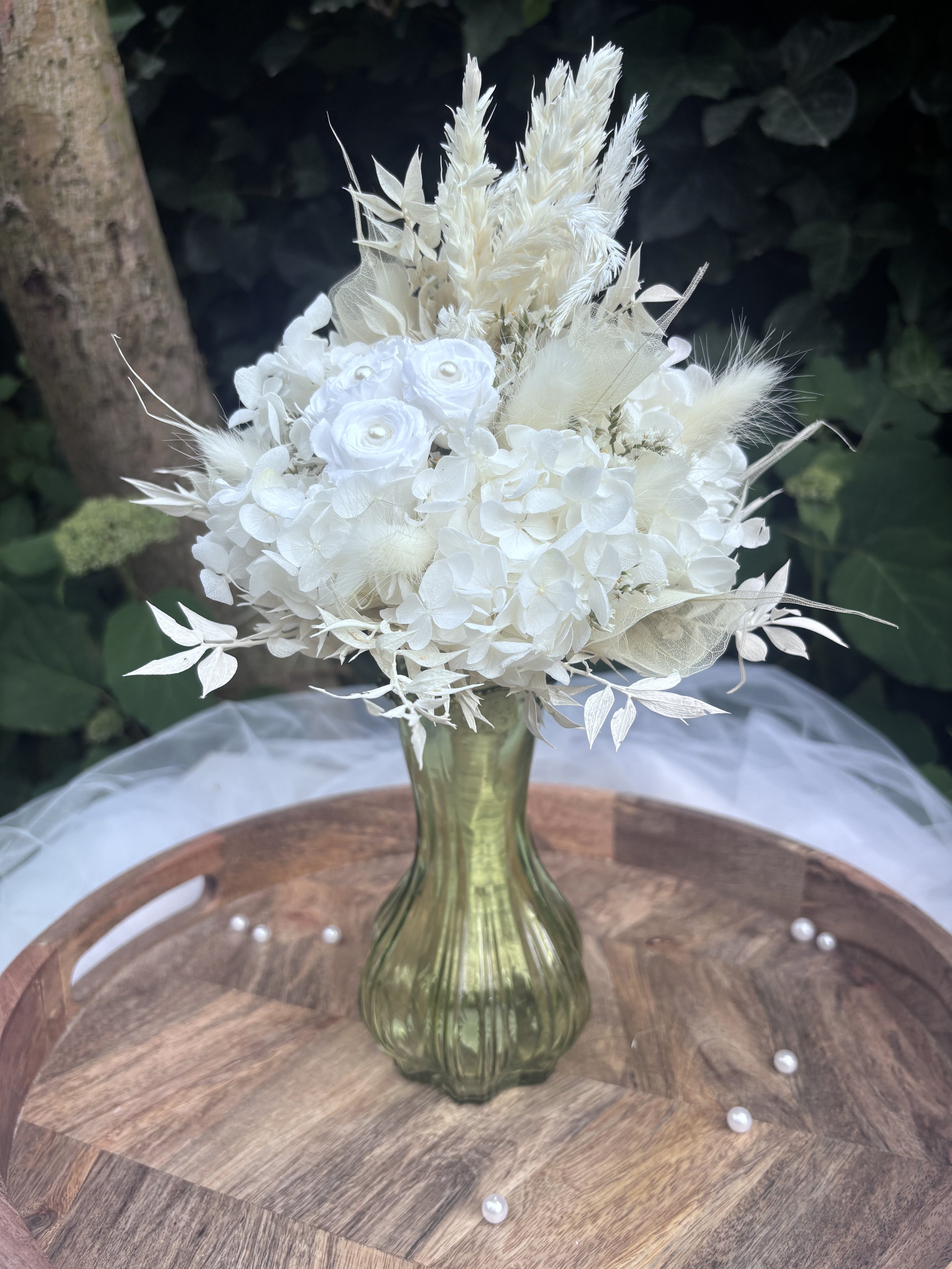 Bouquet de mariée en fleurs séchées et stabilisées blanches, réalisé artisanalement dans un esprit bohème chic et romantique. Cette création florale associe hortensias stabilisés, roses éternelles ornées de perles, arums délicats, feuillages blanchis