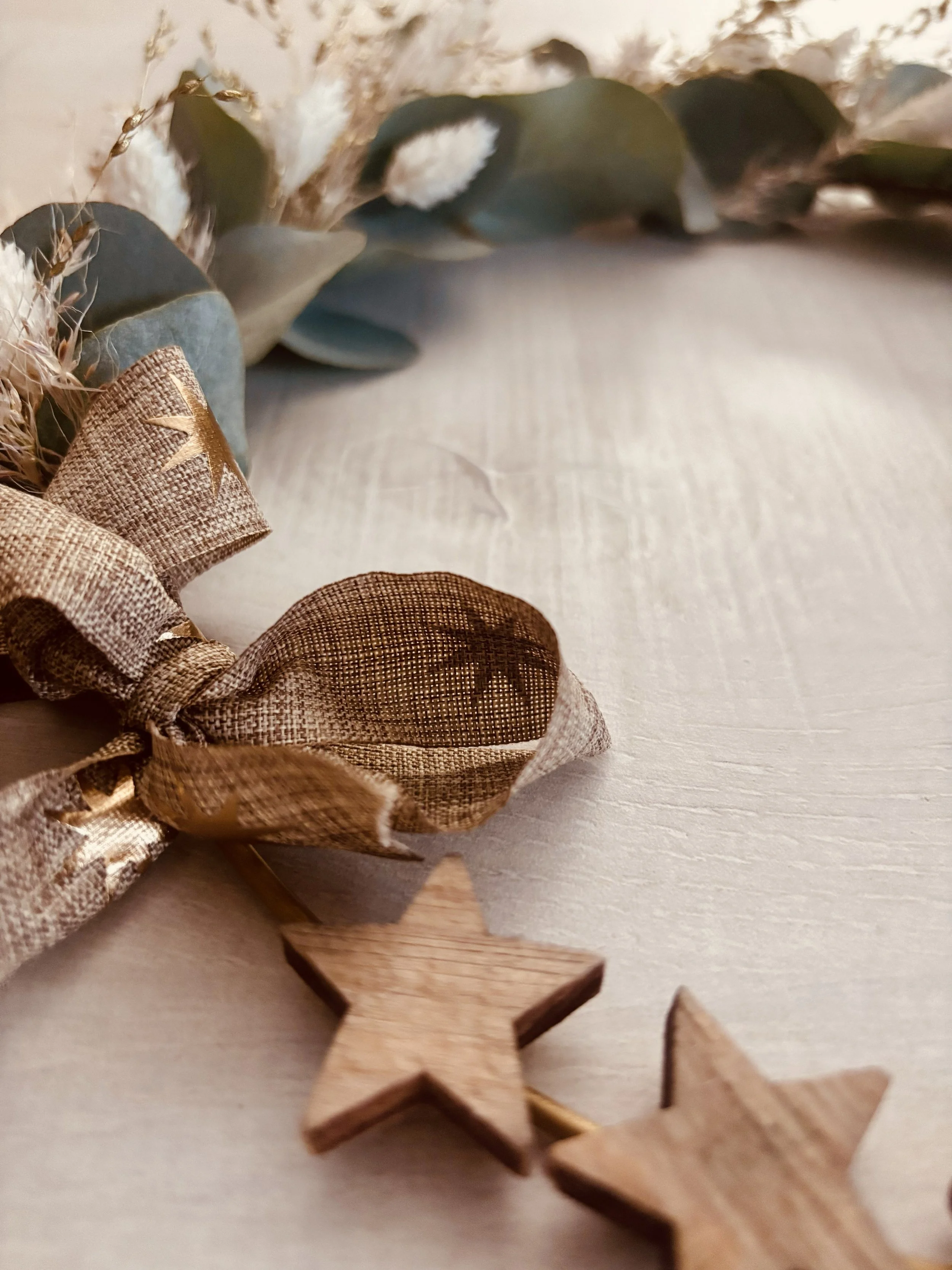 Décorations de Noël avec des étoiles en bois, un ruban en tissu doré et des plantes vertes et blanches.