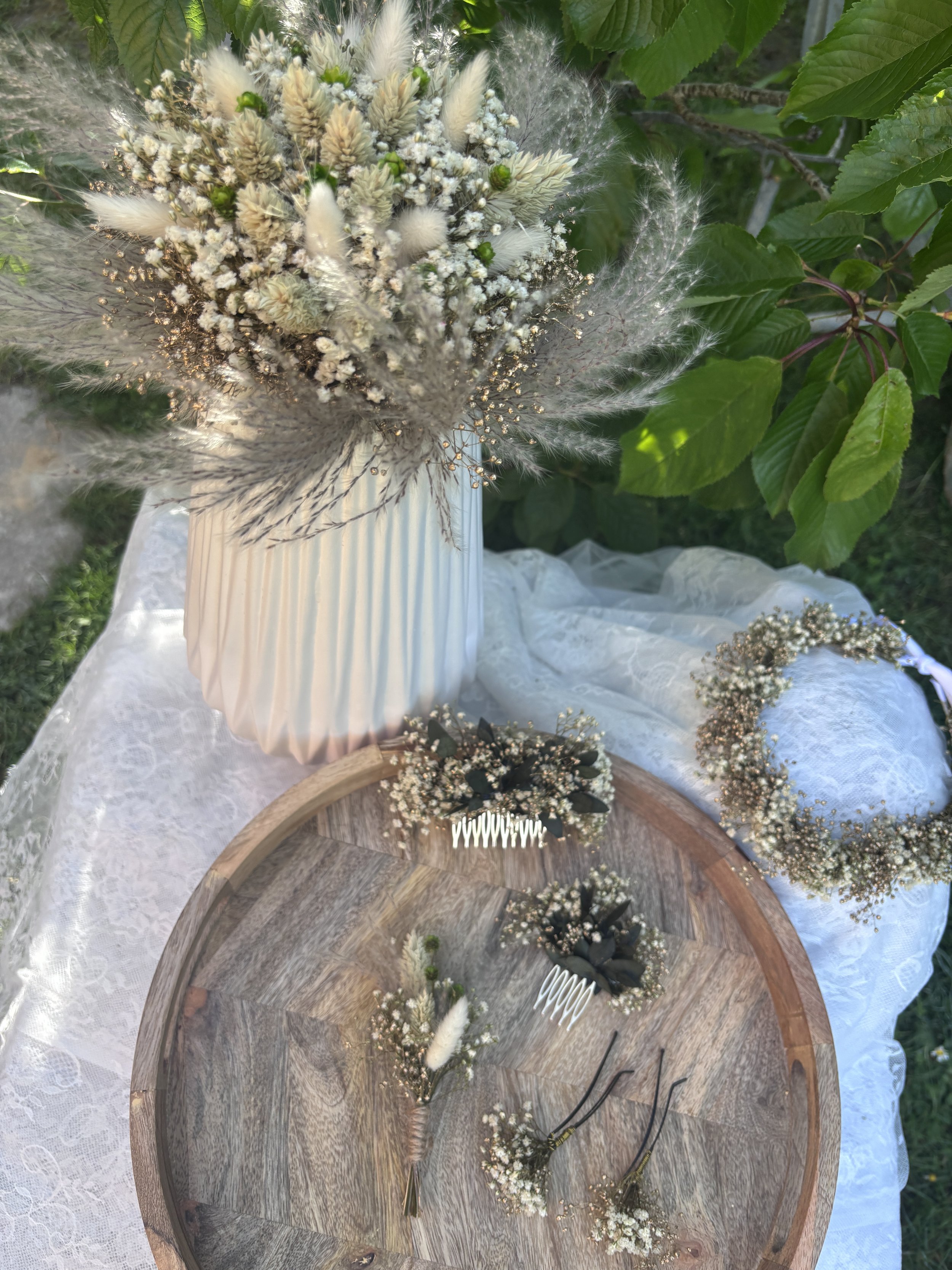 Un bouquet de fleurs blanches, dans un vase blanc, posé sur une surface en bois, avec des feuilles vertes en arrière-plan.