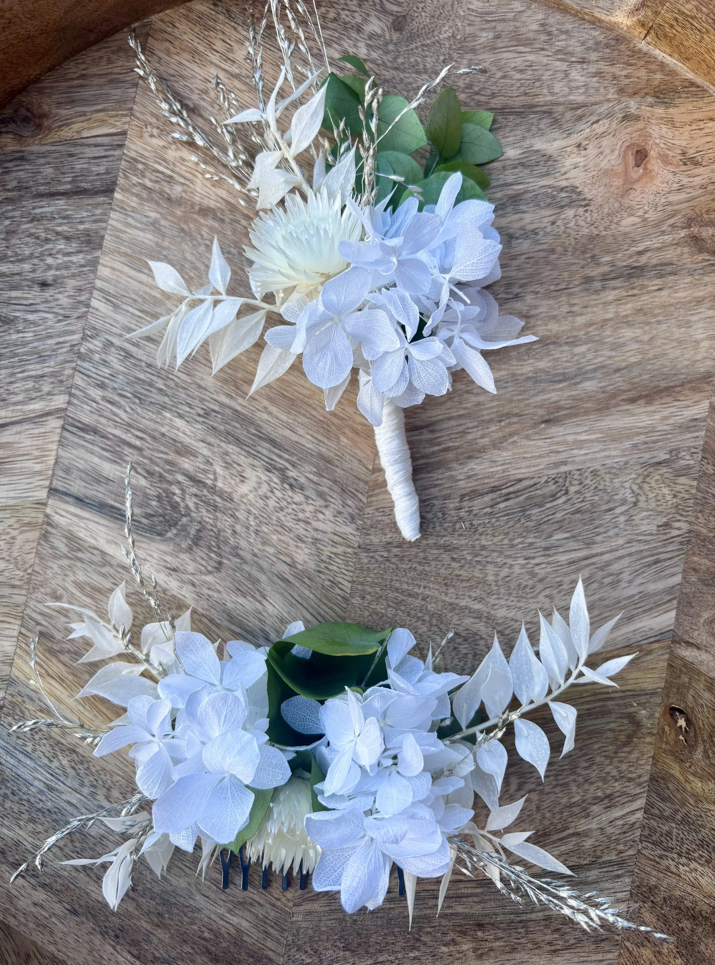 Deux bouquets de fleurs artificielles blanches avec des feuilles vertes, posés sur un plancher en bois, photographed from above.