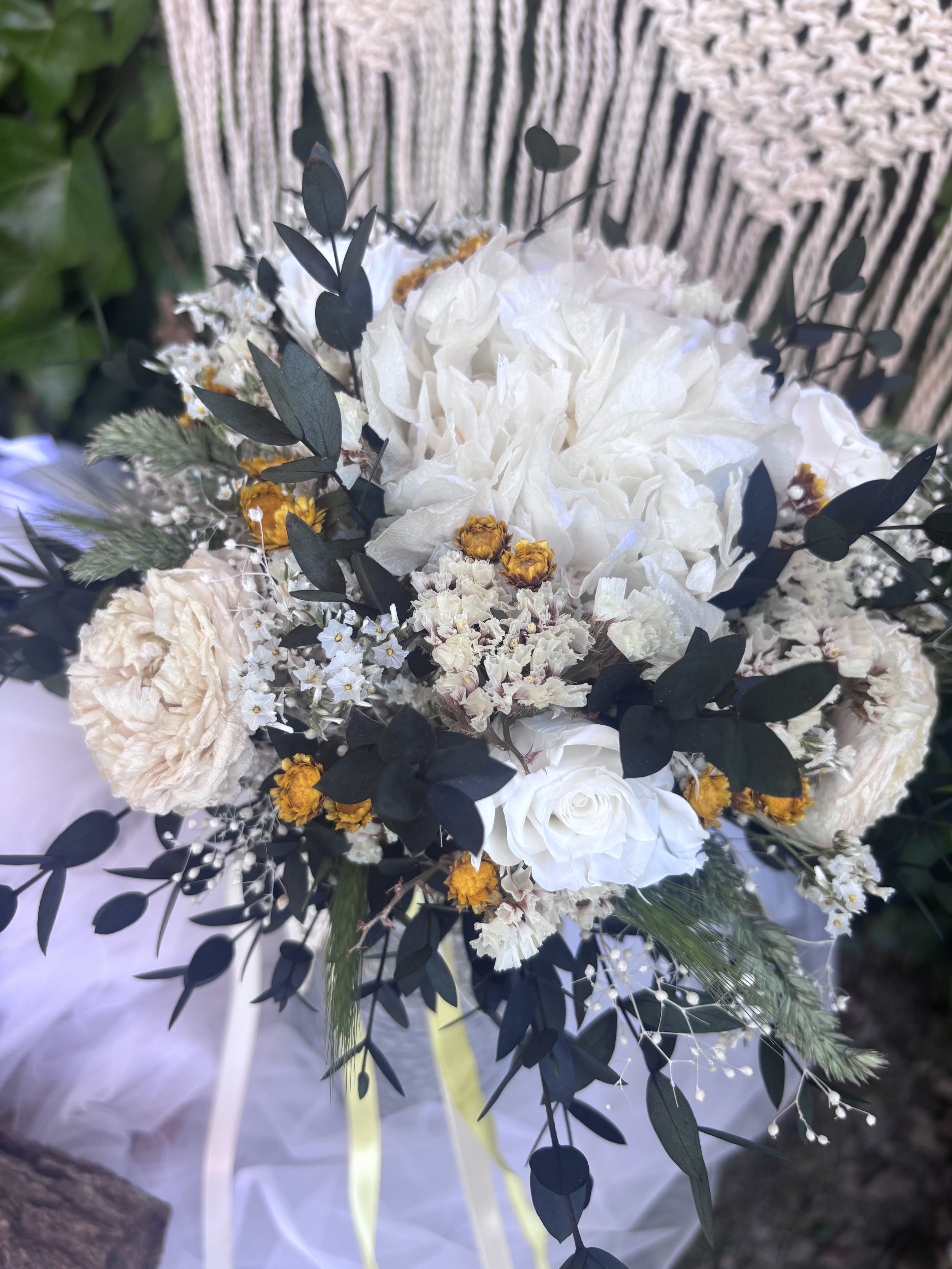 Bouquet de mariée bohème en fleurs séchées et stabilisées, réalisé à la main dans des tons ivoire, blanc cassé, crème et jaune doré. Cette création florale associe hortensia stabilisé, roses éternelles blanches, renoncules séchées, statice, graminées