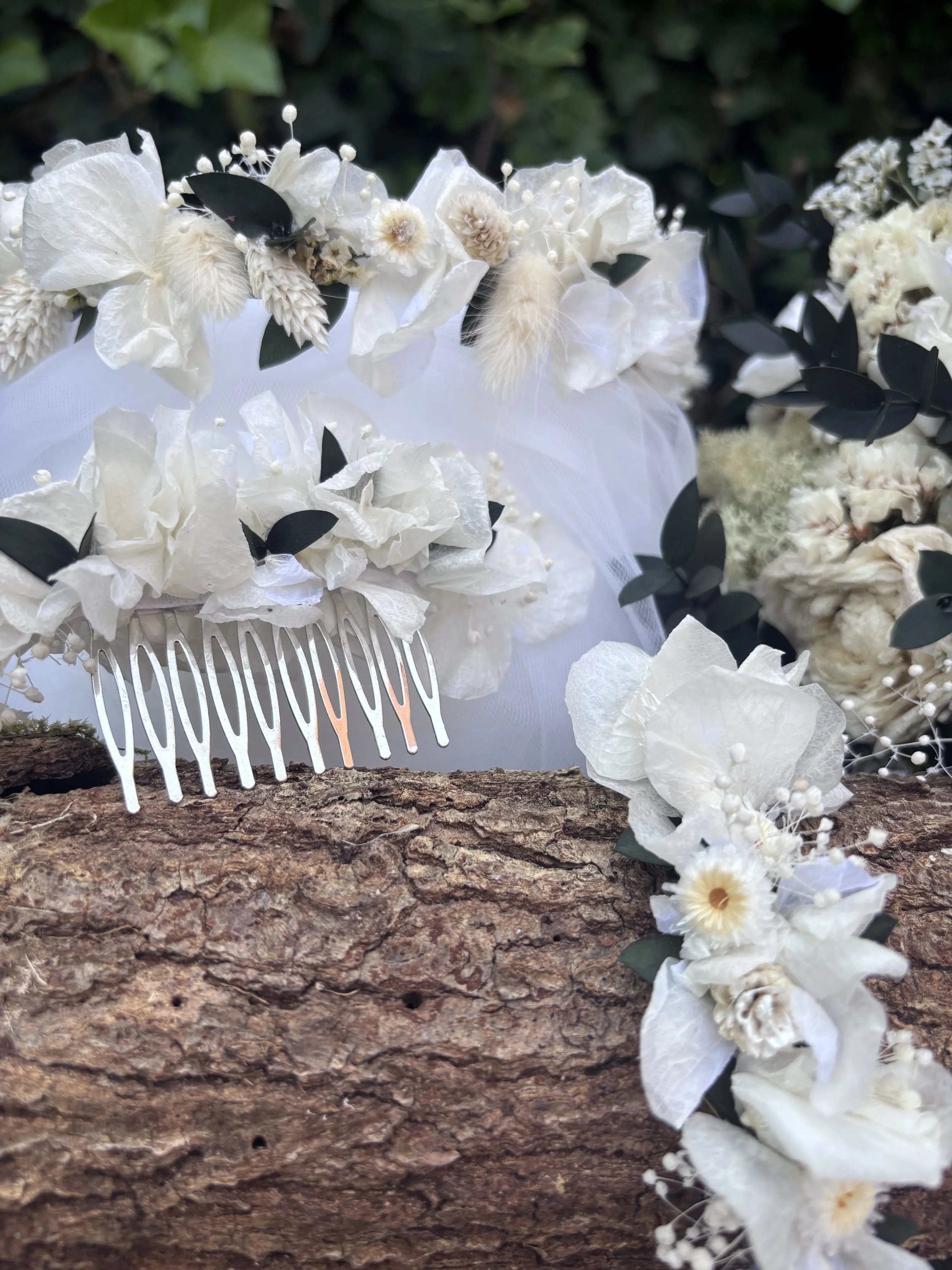 Couronne de fleurs blanches avec feuilles vertes foncées, disposée sur une branche d'écorce naturelle.