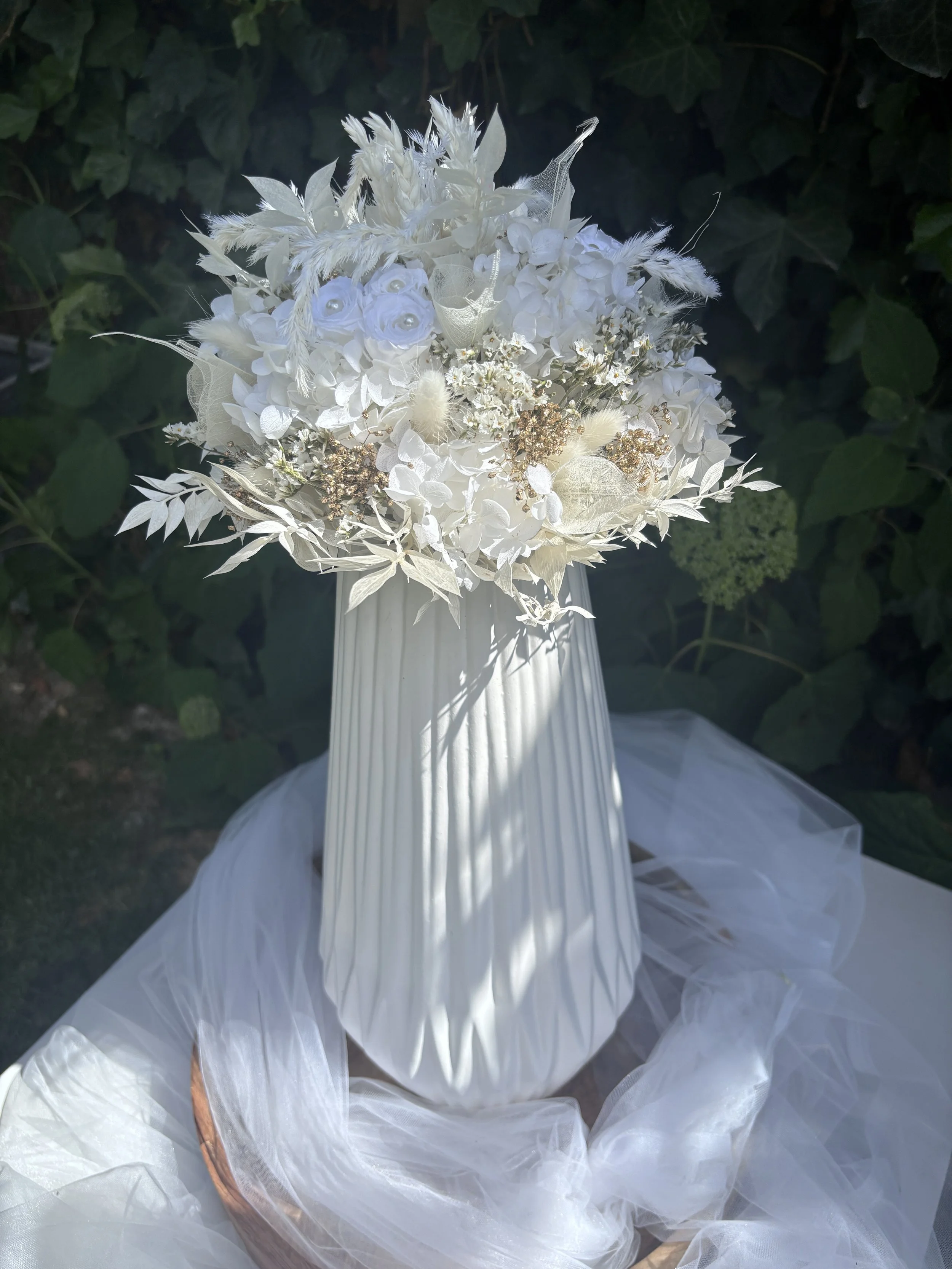 Ce bouquet de mariée en fleurs séchées et stabilisées associe hortensias blancs, renoncules stabilisées, graminées aériennes et délicates touches nacrées pour un rendu élégant, romantique et intemporel. Réalisé à la main dans mon atelier à Saint-Saul