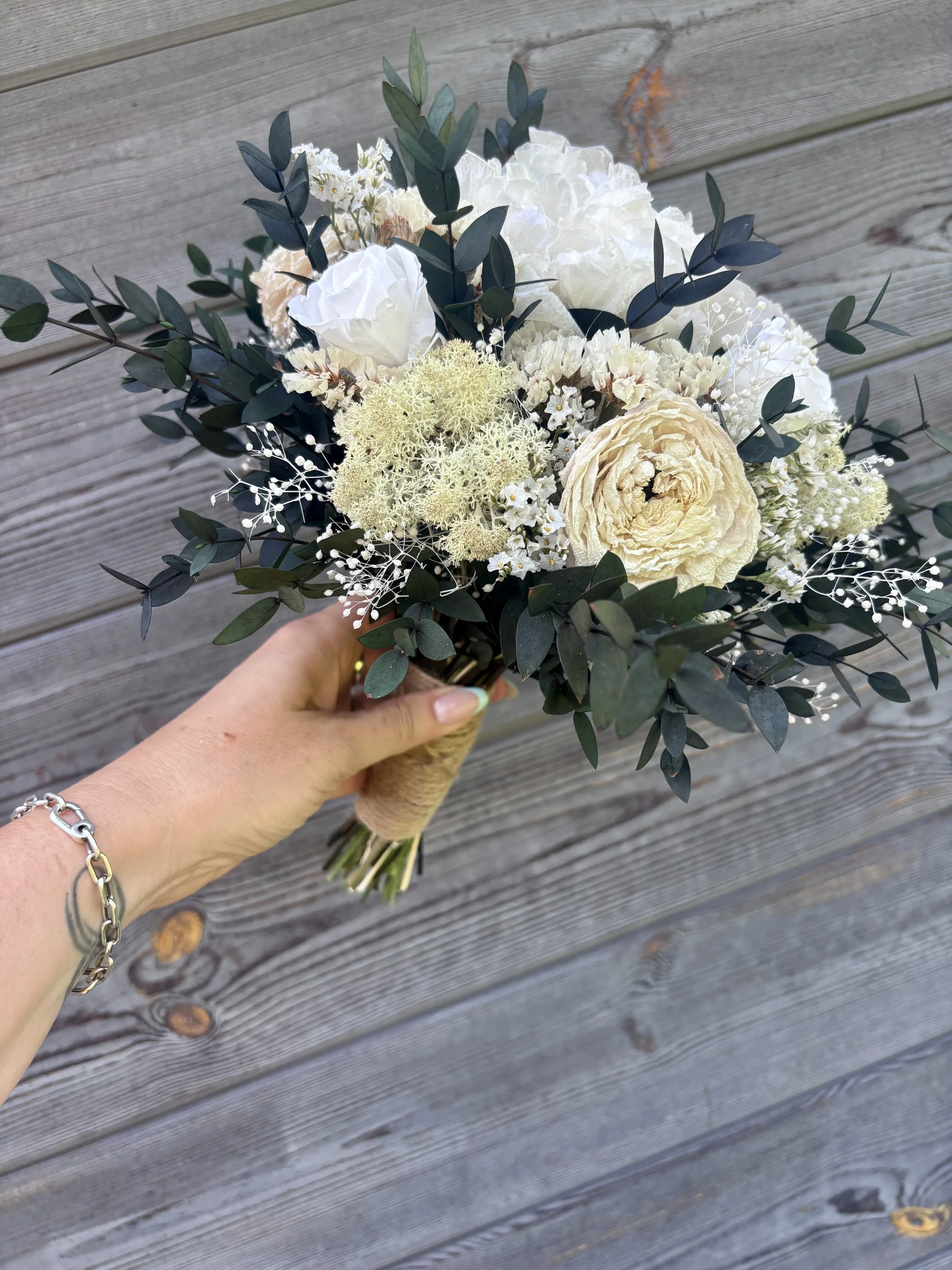 Bouquet de mariée bohème chic en fleurs séchées et stabilisées, composé de pivoines blanches, roses stabilisées, statice blanc, mousse végétale et feuillage d’eucalyptus noir. Cette création artisanale associe élégance, douceur et caractère pour un m