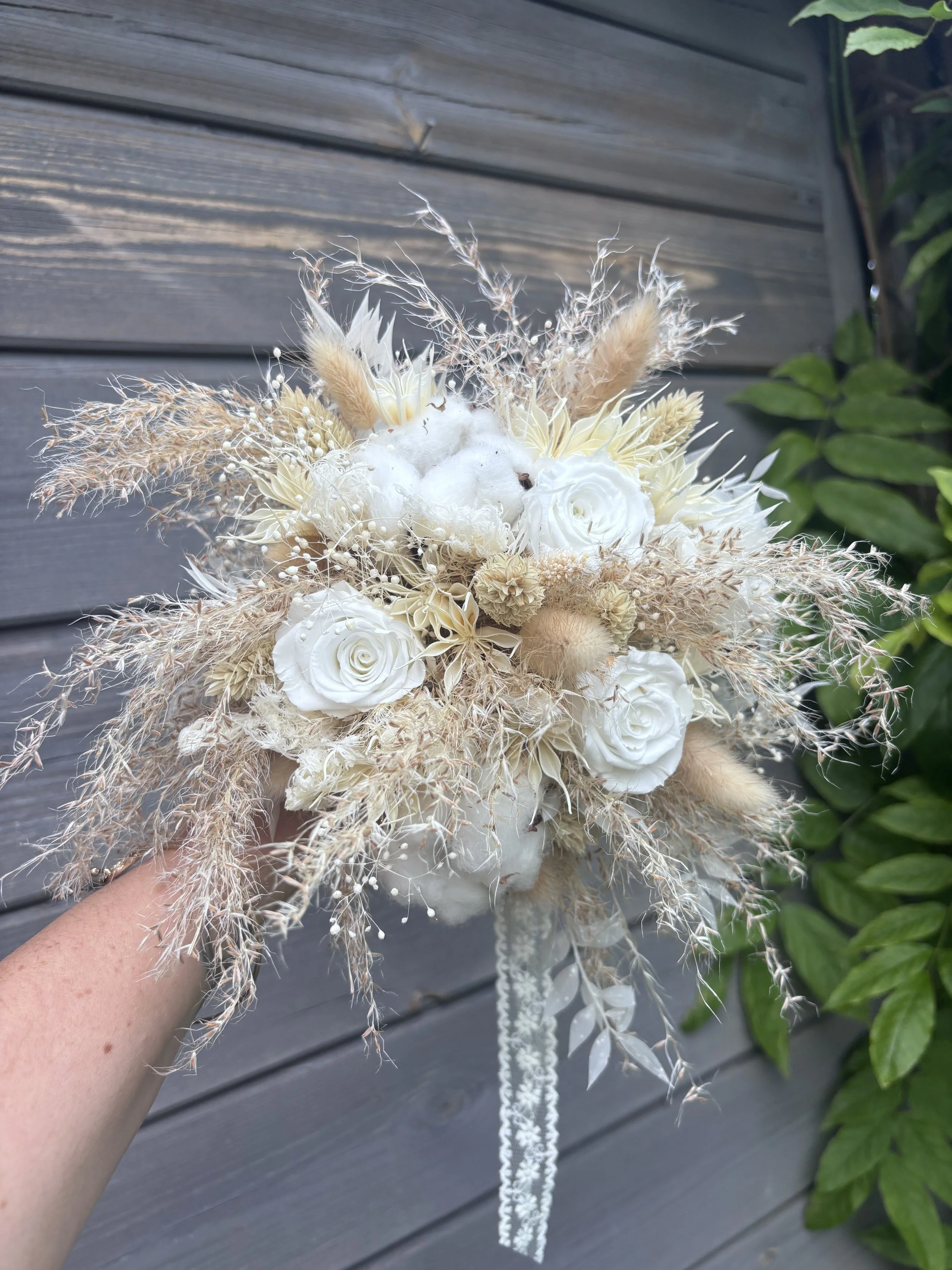 Bouquet de mariée bohème composé de fleurs séchées et stabilisées dans des tons blanc cassé, ivoire et beige naturel. Réalisé à la main par L’Atelier Fleurs & Sens à Saint-Saulve, près de Valenciennes, ce bouquet associe roses stabilisées, coton, gra