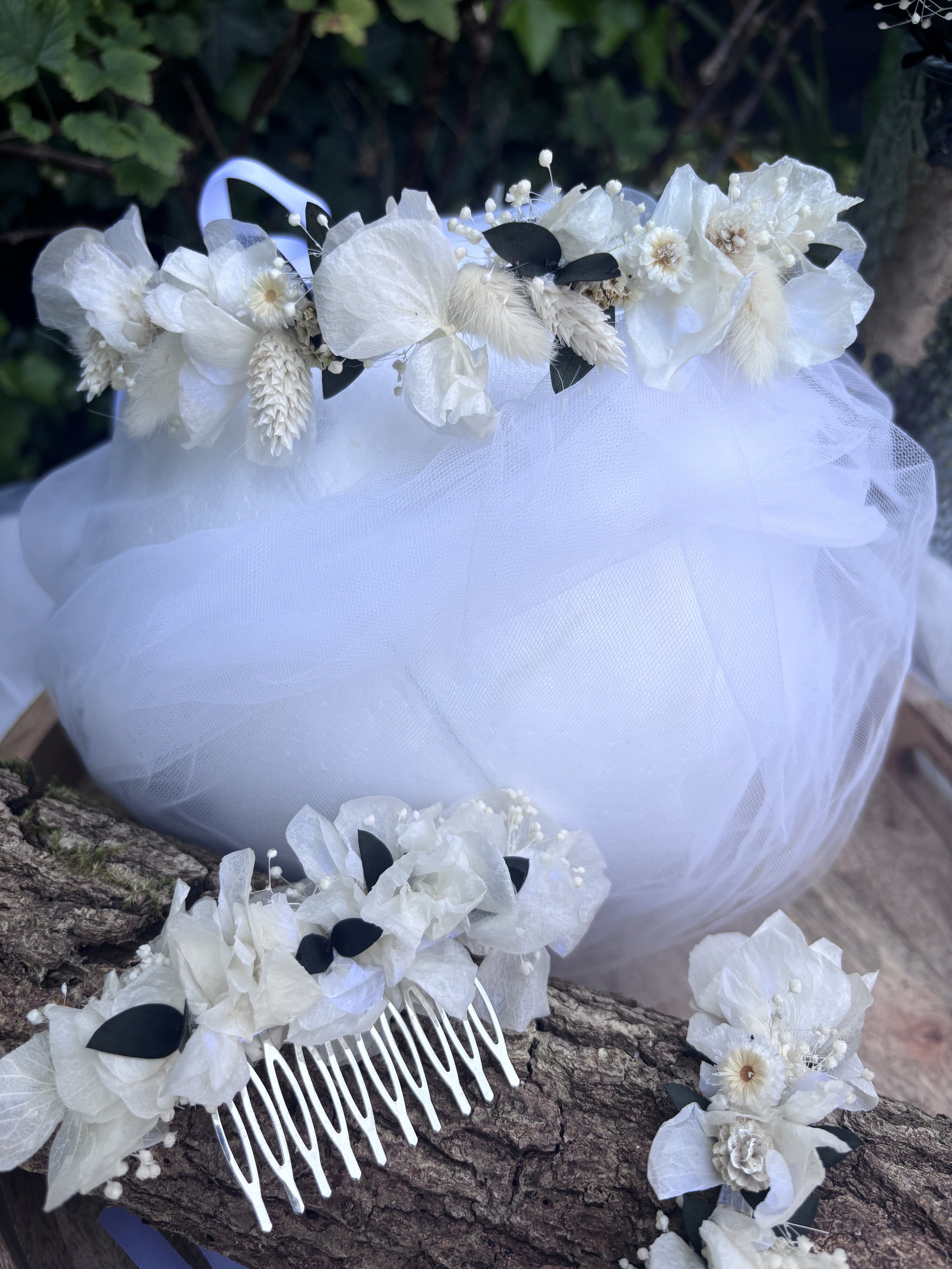 Une démonstration florale blanche composée de fleurs, de feuilles sombres et d'une toile blanche, déposée sur une branche d'arbre.