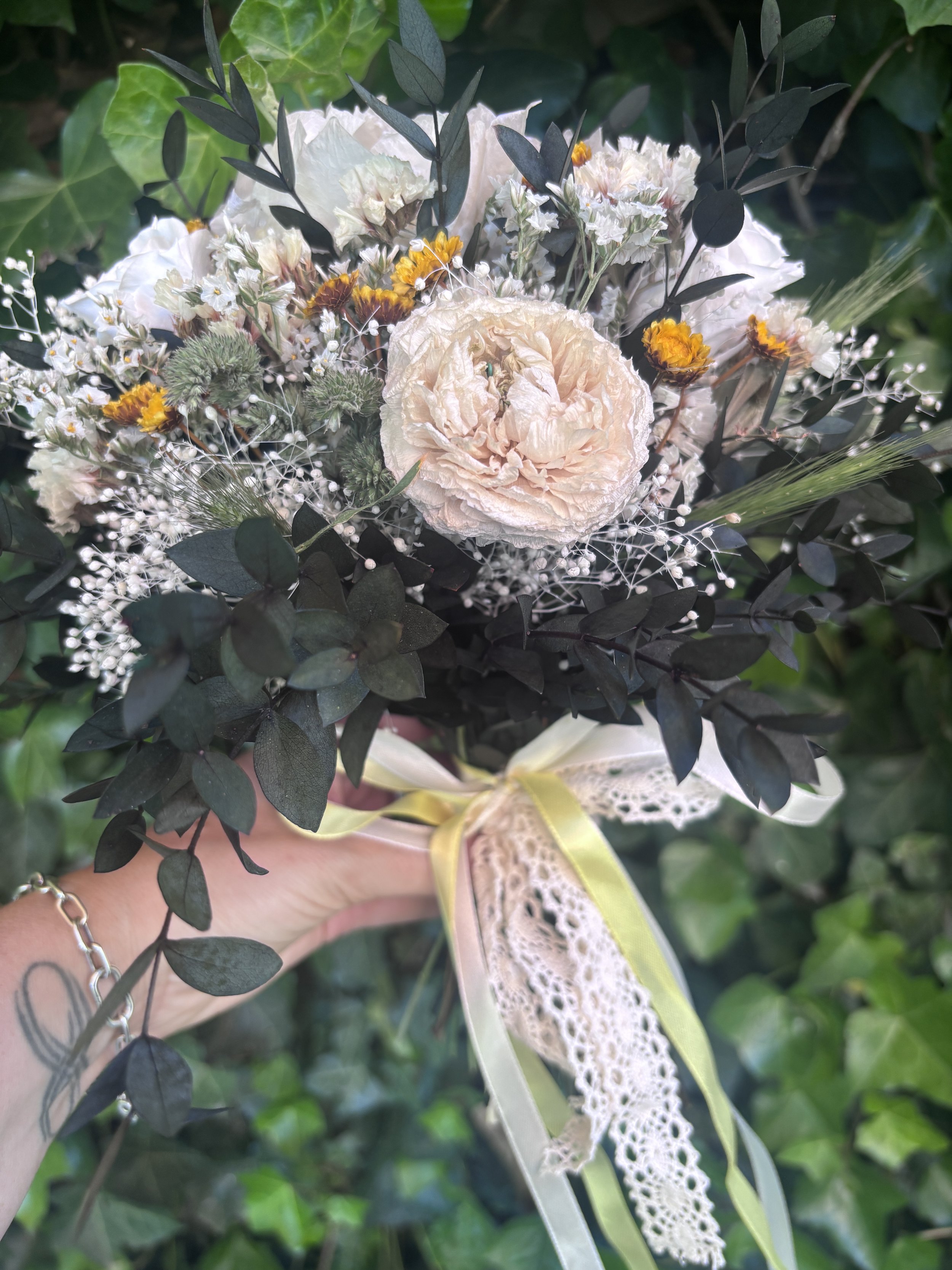Bouquet de mariée bohème en fleurs séchées et stabilisées, réalisé à la main dans des tons ivoire, blanc cassé, crème et jaune doré. Cette création florale associe hortensia stabilisé, roses éternelles blanches, renoncules séchées, statice, graminées