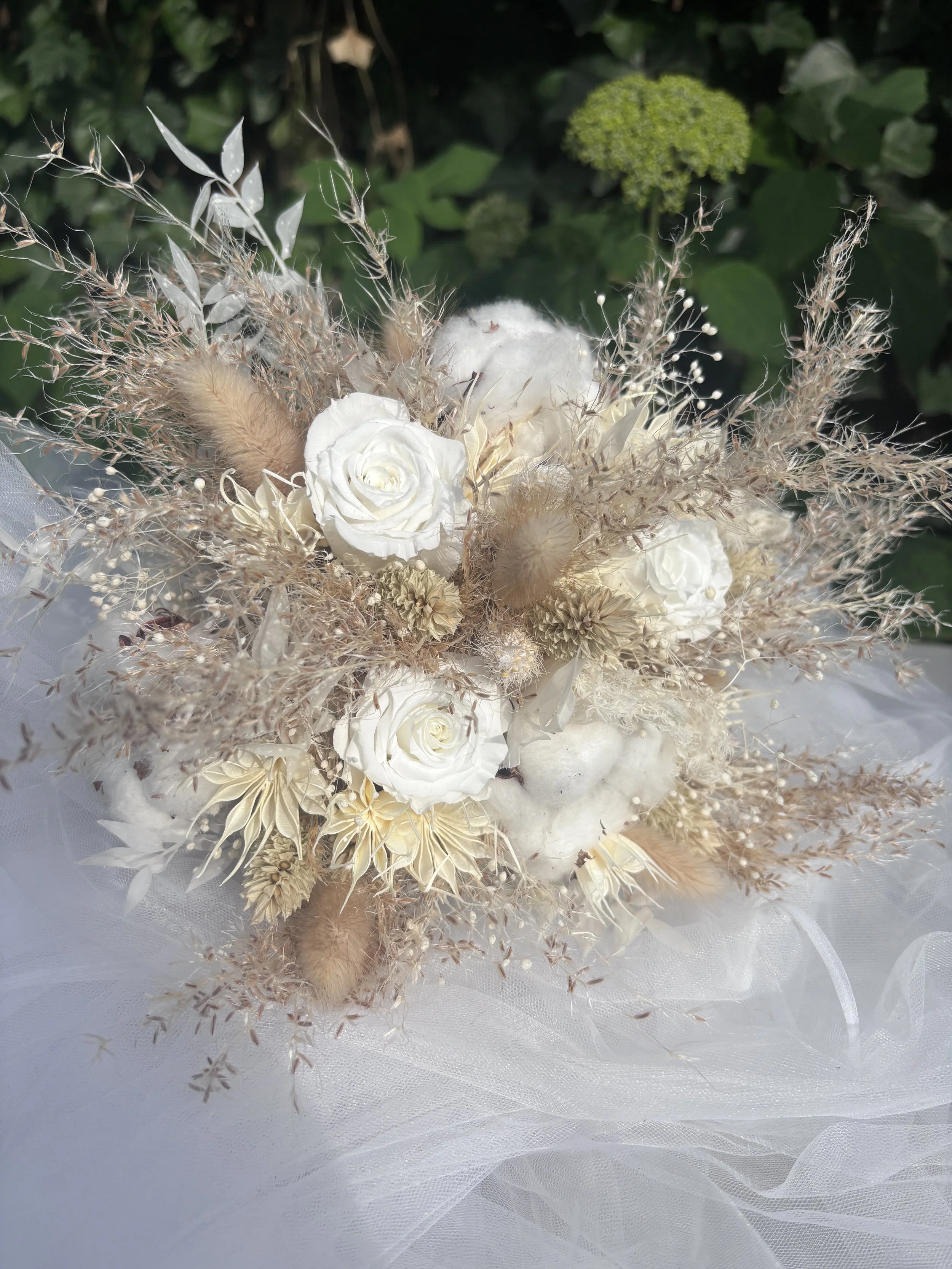 Bouquet de mariée bohème composé de fleurs séchées et stabilisées dans des tons blanc cassé, ivoire et beige naturel. Réalisé à la main par L’Atelier Fleurs & Sens à Saint-Saulve, près de Valenciennes, ce bouquet associe roses stabilisées, coton, gra