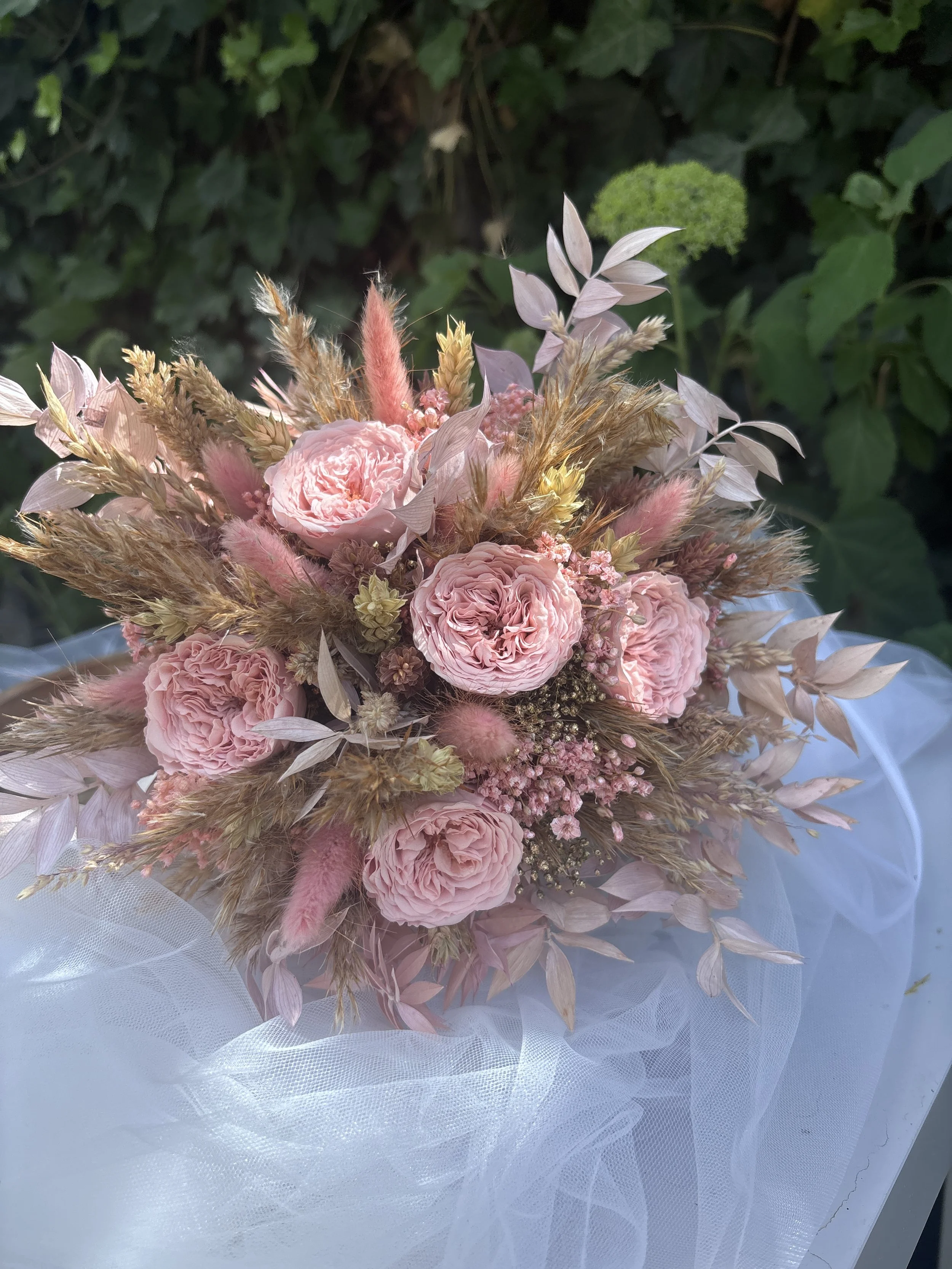 Bouquet de mariée bohème en fleurs séchées et stabilisées dans des tons rose poudré, nude et beige naturel. Création artisanale réalisée par L’Atelier Fleurs & Sens à Saint-Saulve, près de Valenciennes. Composé de roses stabilisées premium, lagurus r