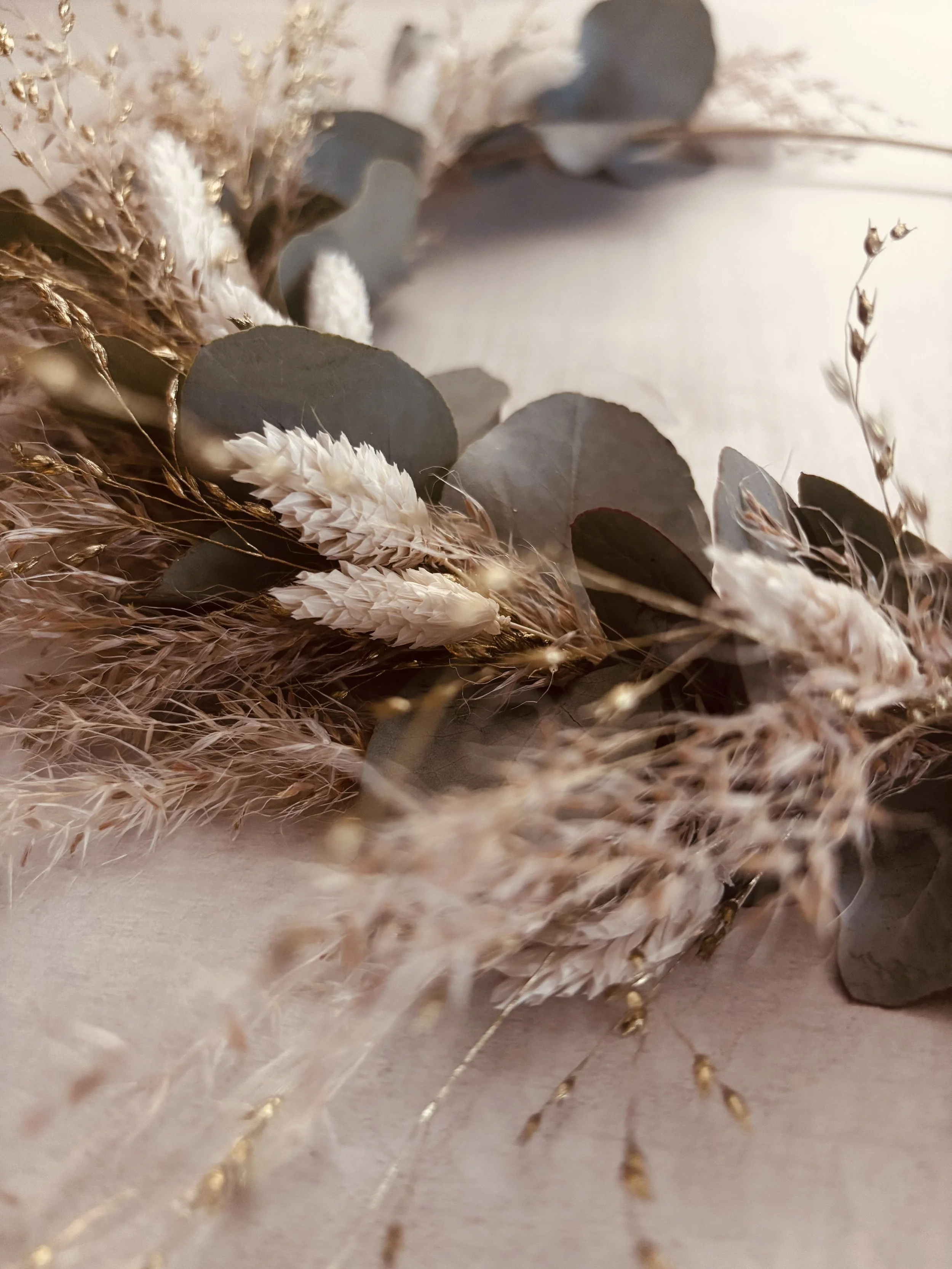 Rassemblement de fleurs séchées de différentes textures et couleurs, comprenant des feuillages gris, des pampas blanches et des éléments végétaux fins et dorés, disposés en un arrangement décoratif.