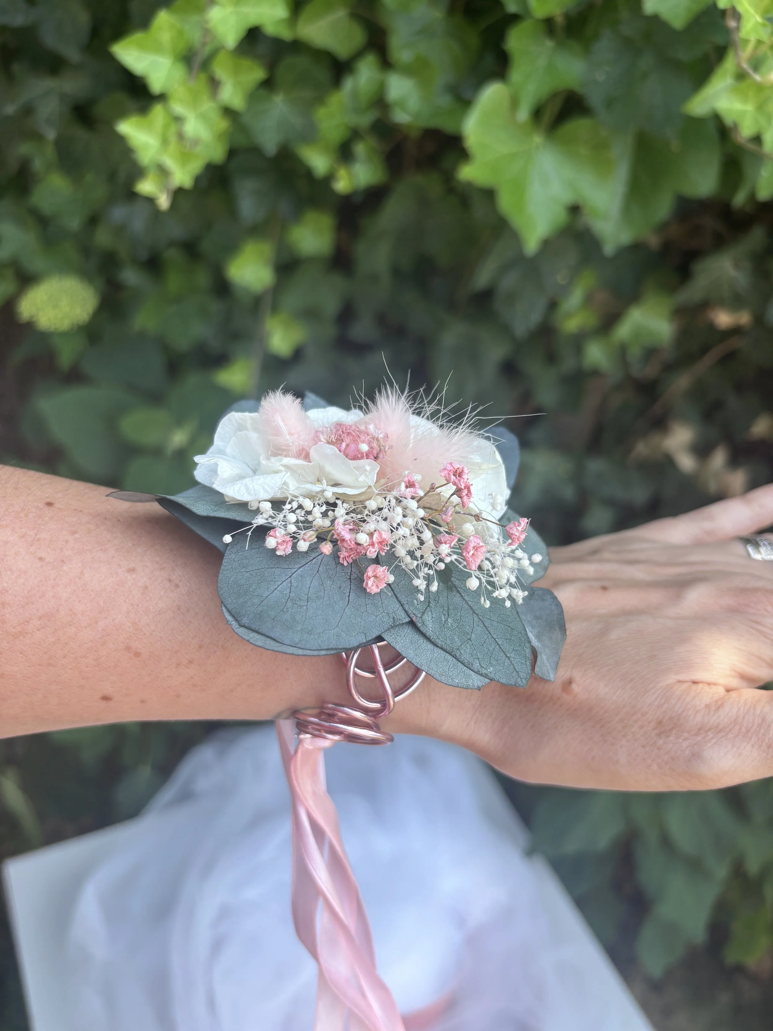 Bracelet fleuri pour mariage, réalisé en fleurs séchées et stabilisées dans des teintes rose poudré, blanc naturel et vert eucalyptus. Une manchette florale bohème et délicate, montée sur fil métallique avec ruban satin rose, idéale pour une témoin, 