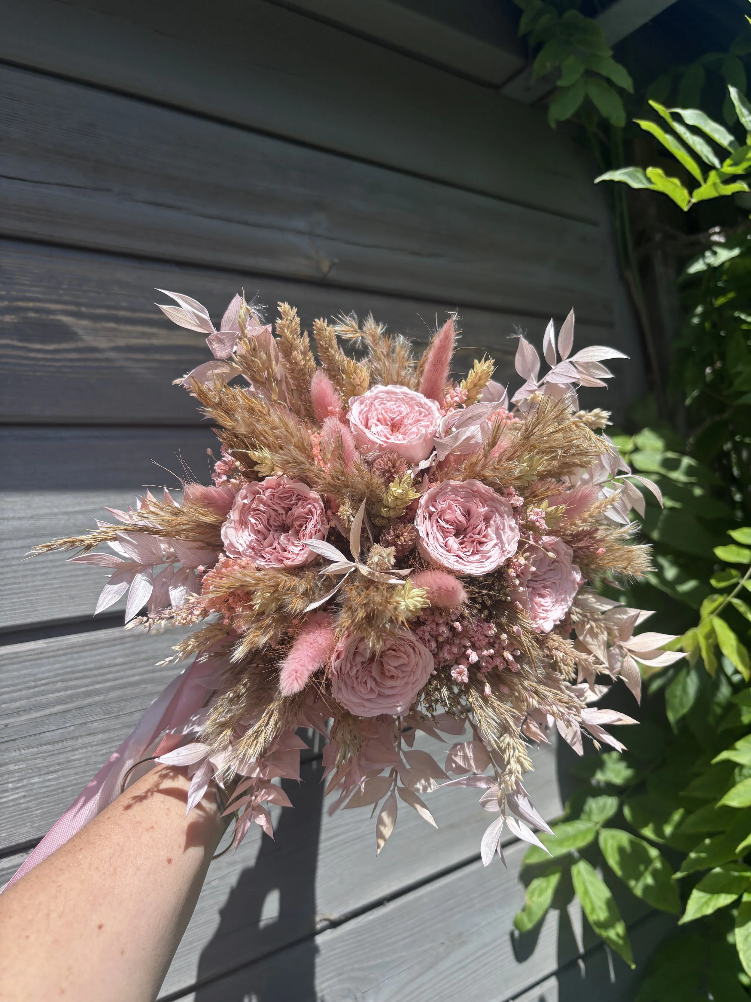 Bouquet de mariée bohème en fleurs séchées et stabilisées dans des tons rose poudré, nude et beige naturel. Création artisanale réalisée par L’Atelier Fleurs & Sens à Saint-Saulve, près de Valenciennes. Composé de roses stabilisées premium, lagurus r