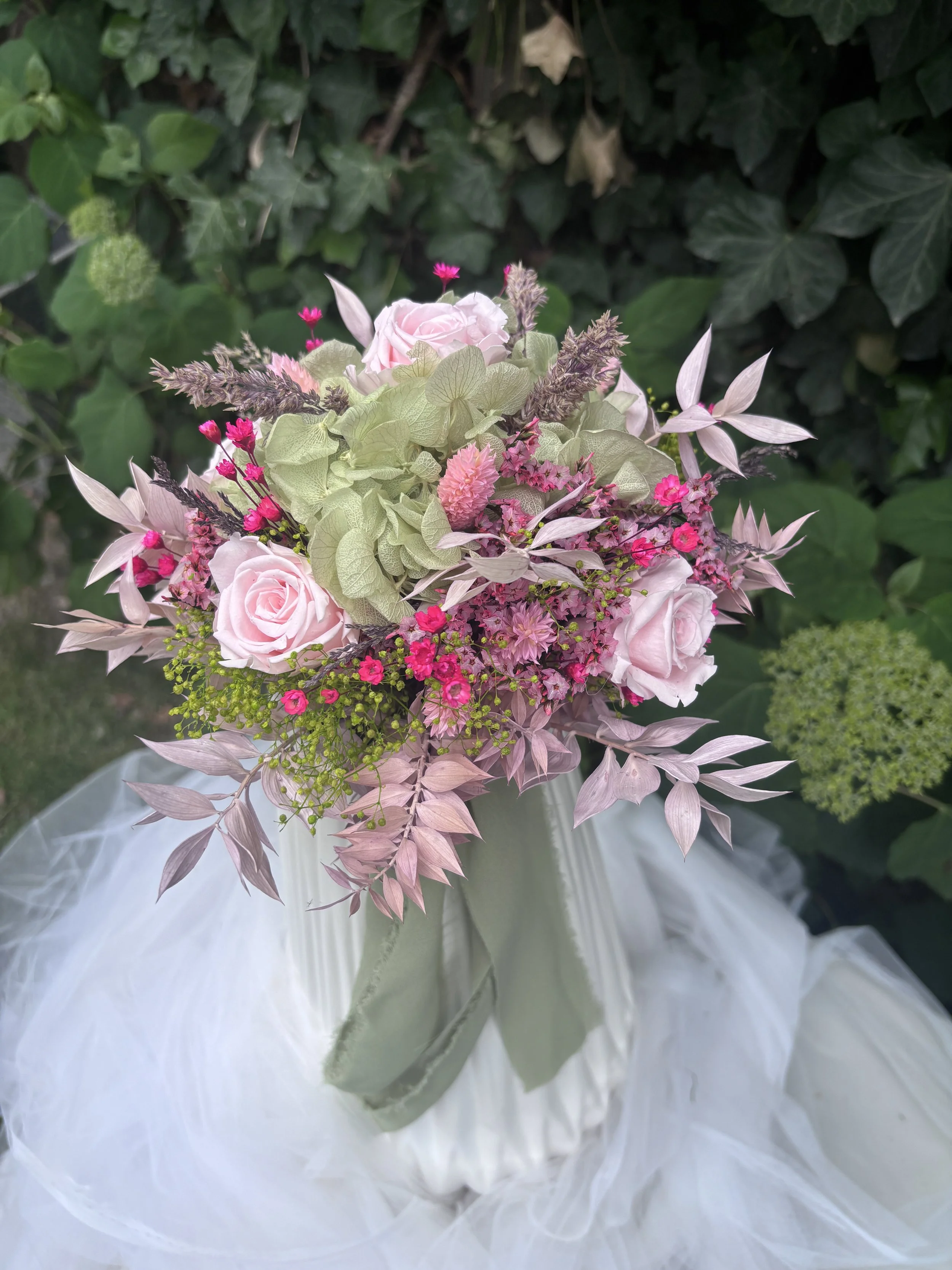 Bouquet de mariée en fleurs séchées et stabilisées aux tons rose poudré, vert sauge et beige naturel, réalisé à la main par L’Atelier Fleurs & Sens près de Valenciennes. Cette création florale bohème et romantique associe hortensia stabilisé, roses s