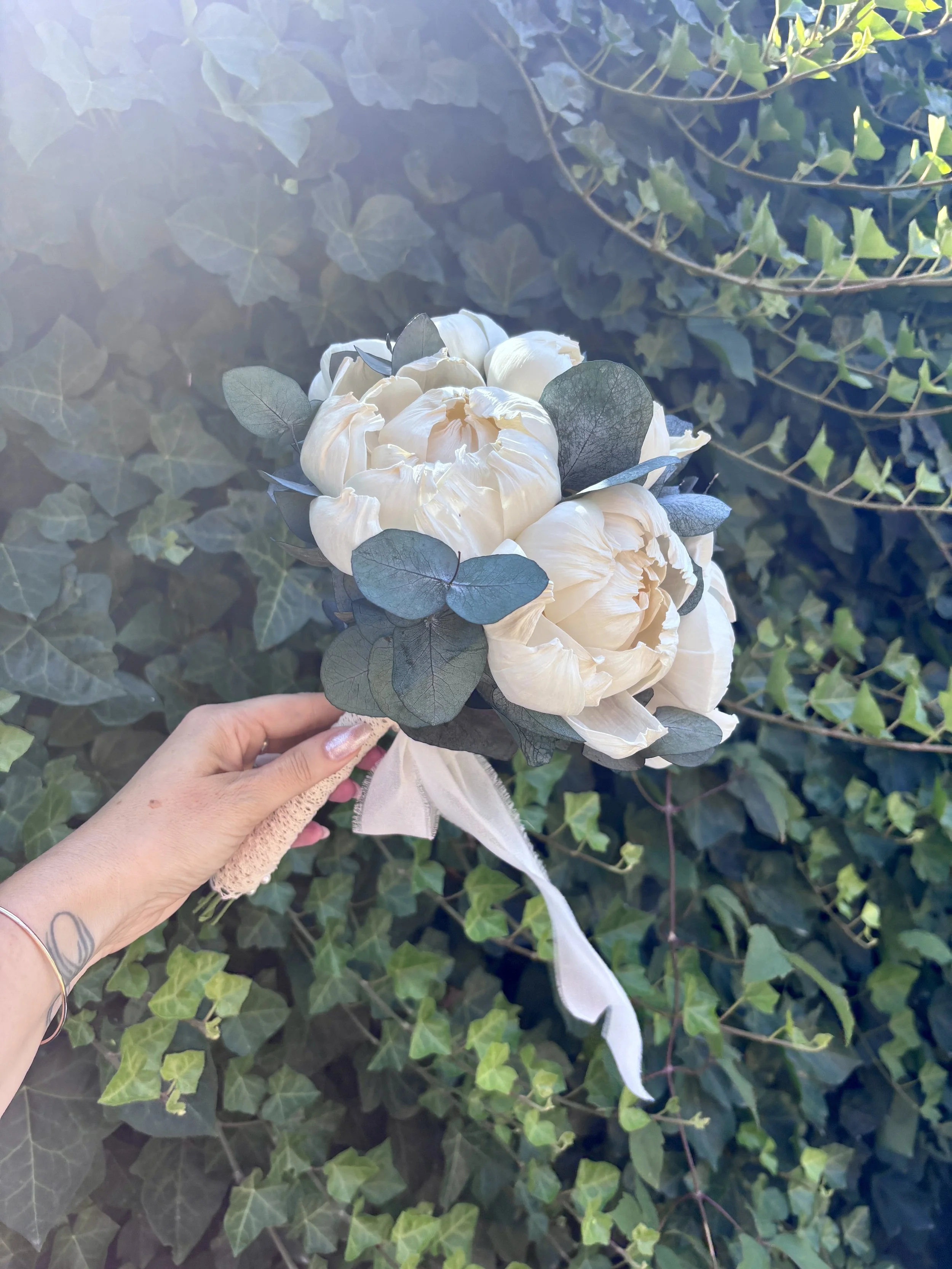 Bouquet de mariée élégant et intemporel composé de grandes pivoines ivoire en bois de Sola, associées à un feuillage d’eucalyptus. Une création florale durable, réalisée artisanalement et personnalisable selon les couleurs du mariage par L’Atelier Fl