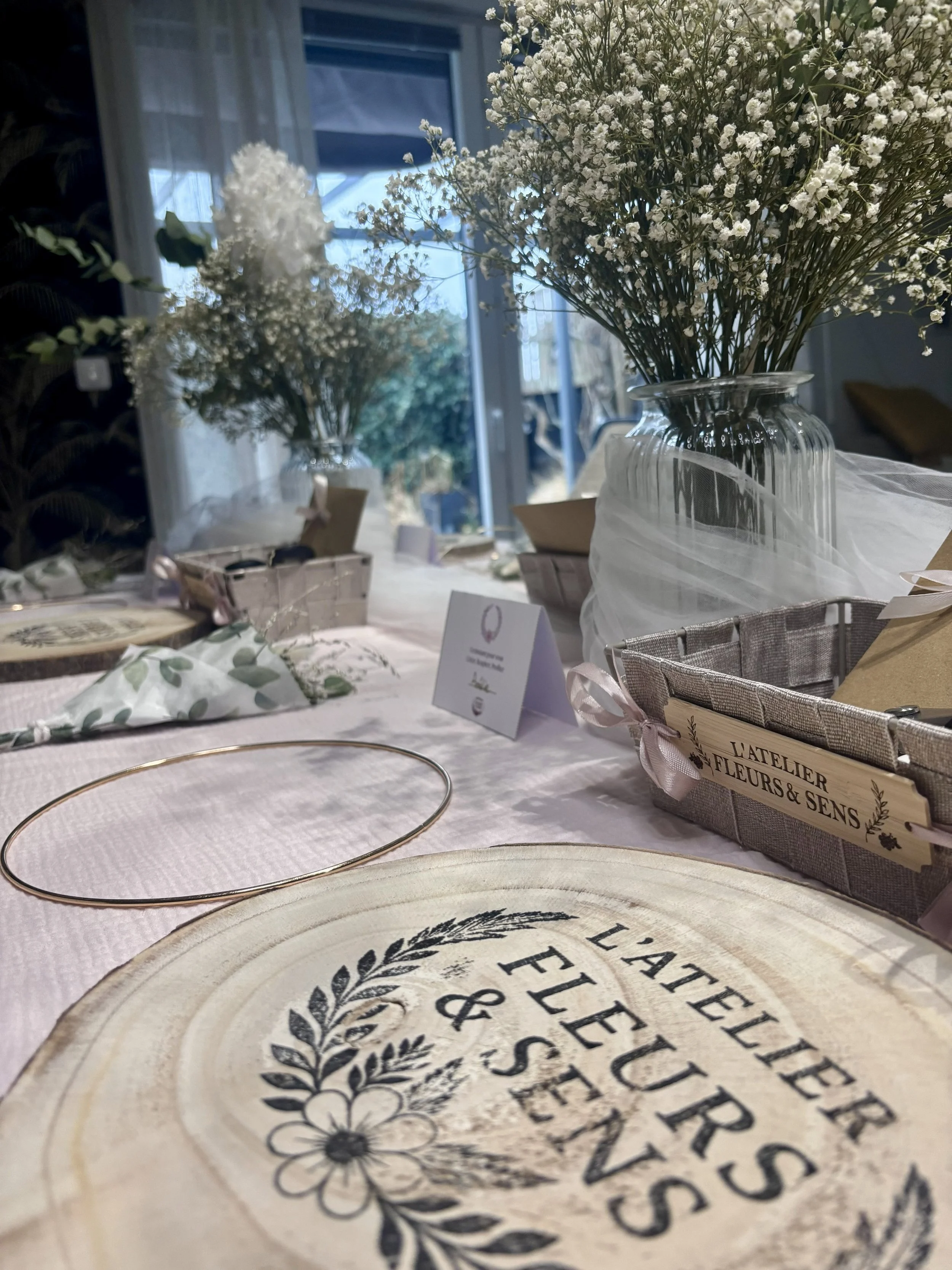 Table décorée avec des bouquets de fleurs blanches, assiettes en bois avec inscription, et petits sacs cadeaux, dans une ambiance lumineuse