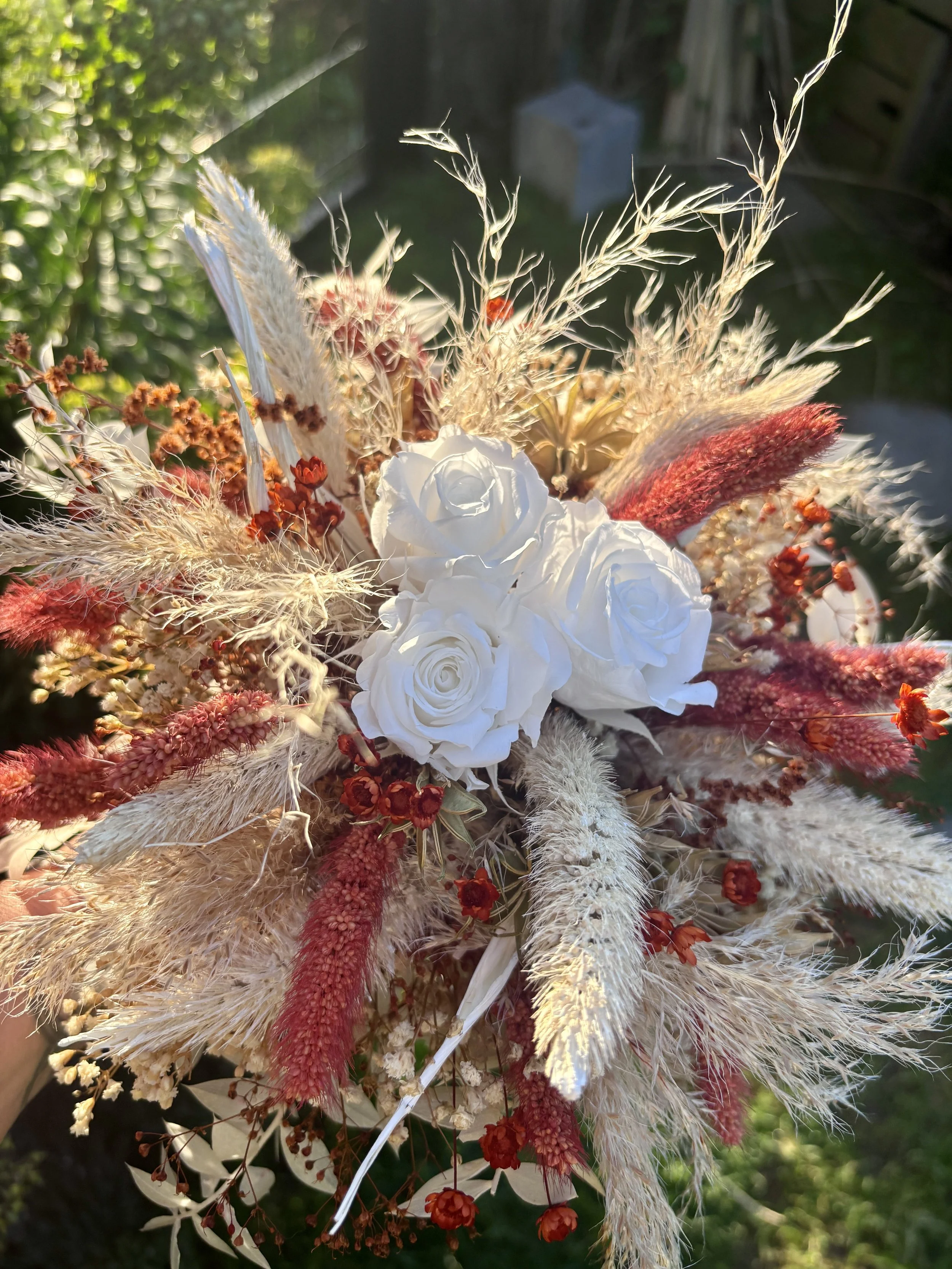 Bouquet de mariée bohème en fleurs séchées et stabilisées aux teintes terracotta, bordeaux, crème et blanc. Cette création florale artisanale associe roses éternelles blanches, pampas, setaria, graminées naturelles et délicates fleurs séchées pour of