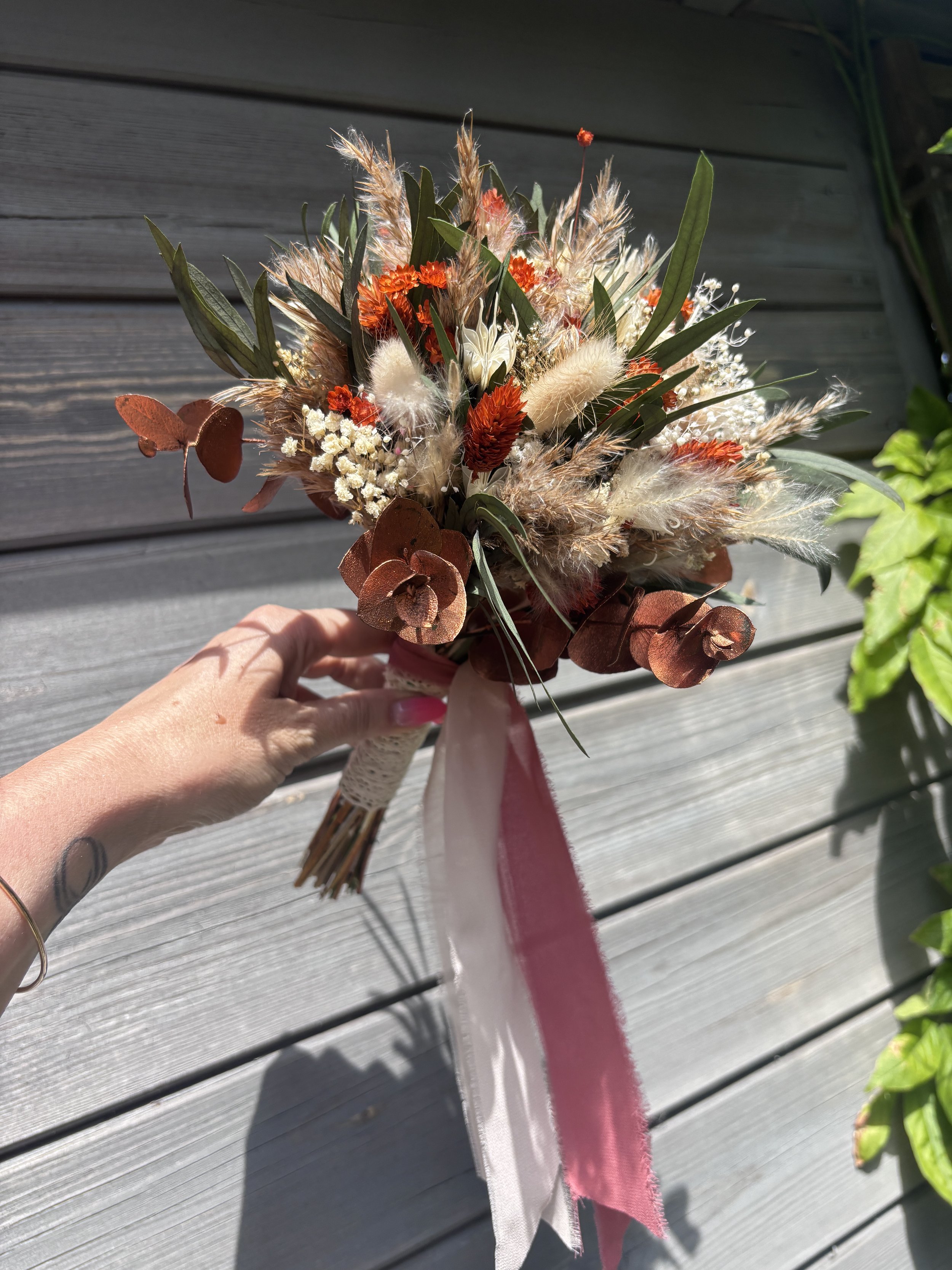 Bouquet de mariée en fleurs séchées et stabilisées dans un style bohème champêtre, composé de gypsophile, lagurus, eucalyptus, fleurs terracotta, touches crème et feuillages aux nuances bordeaux. Une création durable et naturelle, idéale pour un mari