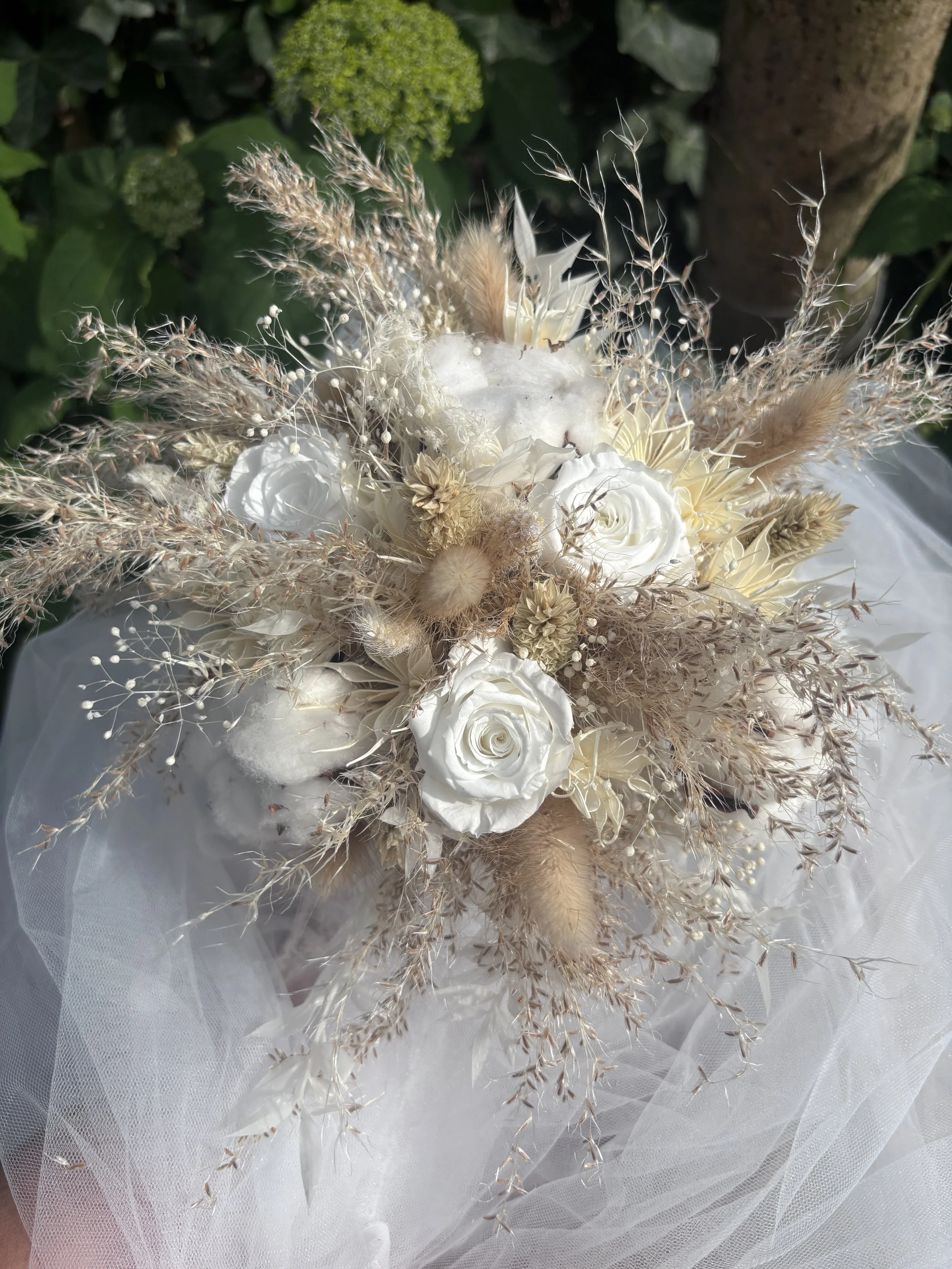 Bouquet de mariée bohème composé de fleurs séchées et stabilisées dans des tons blanc cassé, ivoire et beige naturel. Réalisé à la main par L’Atelier Fleurs & Sens à Saint-Saulve, près de Valenciennes, ce bouquet associe roses stabilisées, coton, gra