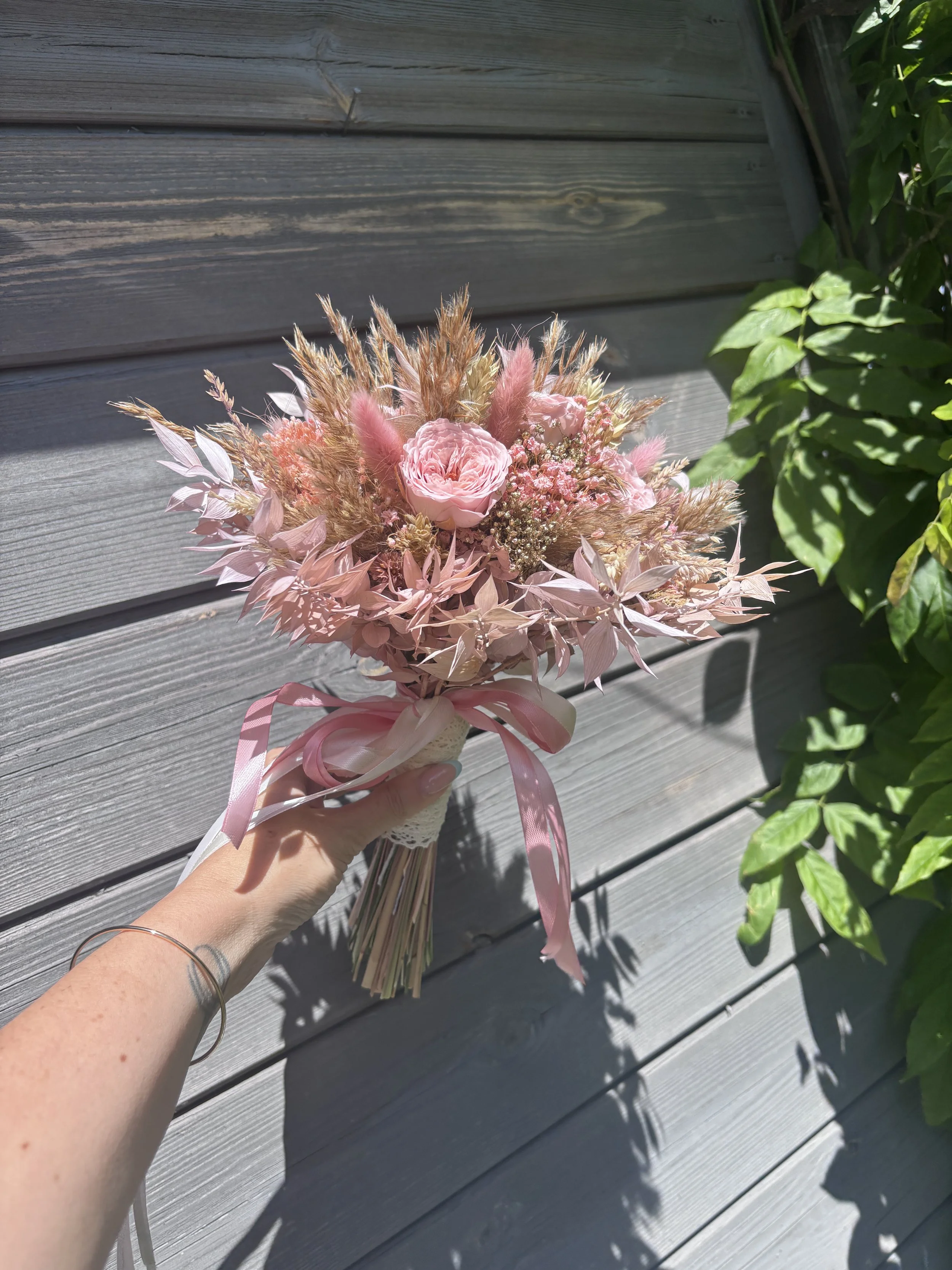 Bouquet de mariée bohème en fleurs séchées et stabilisées dans des tons rose poudré, nude et beige naturel. Création artisanale réalisée par L’Atelier Fleurs & Sens à Saint-Saulve, près de Valenciennes. Composé de roses stabilisées premium, lagurus r