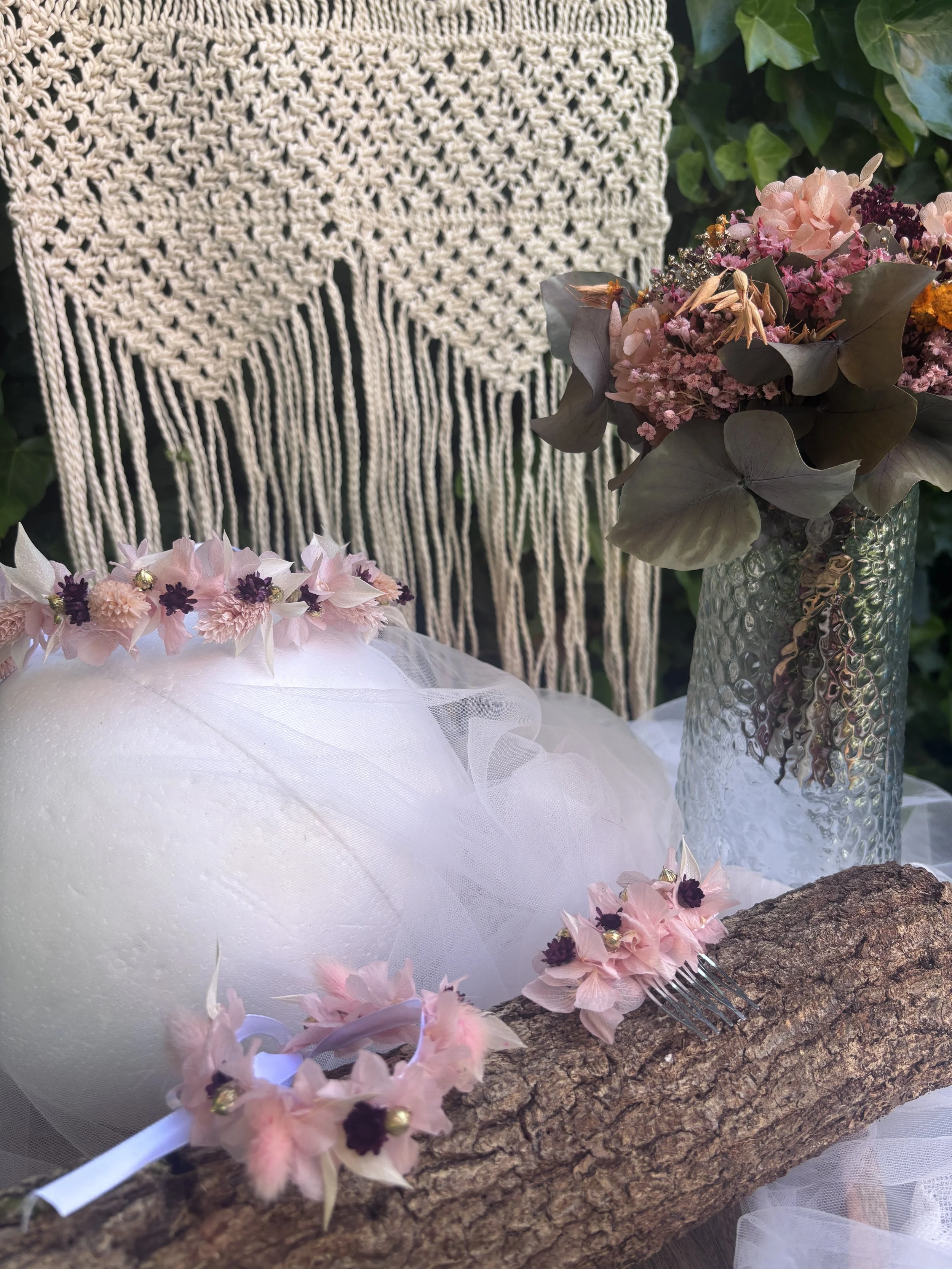 Composition florale avec des fleurs roses, une boule blanche en forme de tête et une branche d'arbre sur une branche d'écorce.