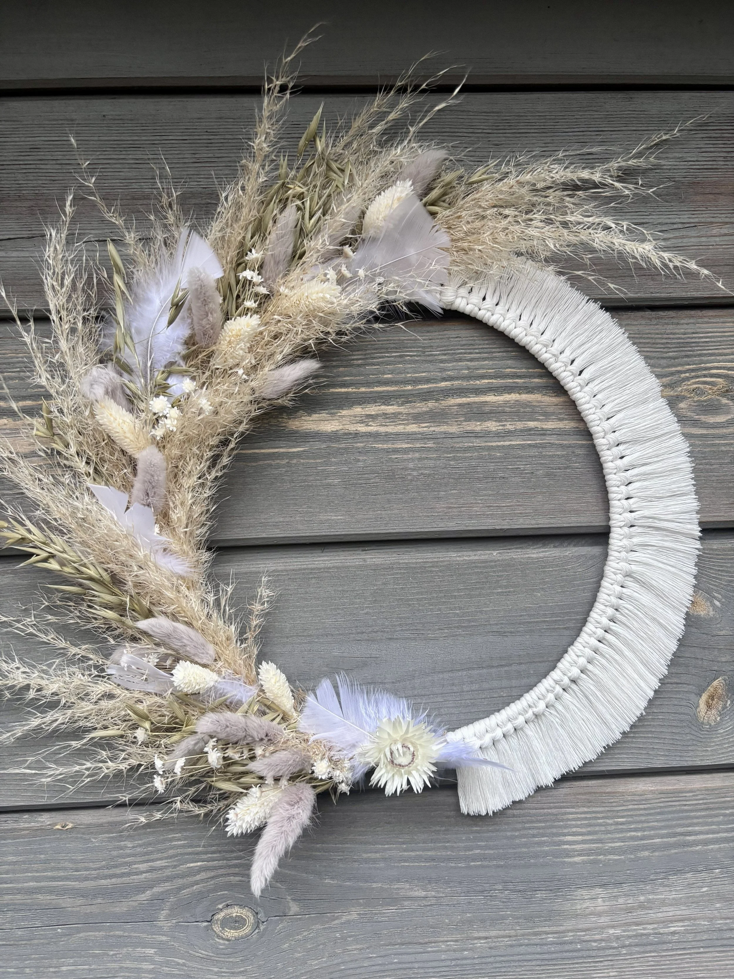 Couronne décorative faite de végétaux secs, plumes et fleurs blanches, fixée sur un fond en bois