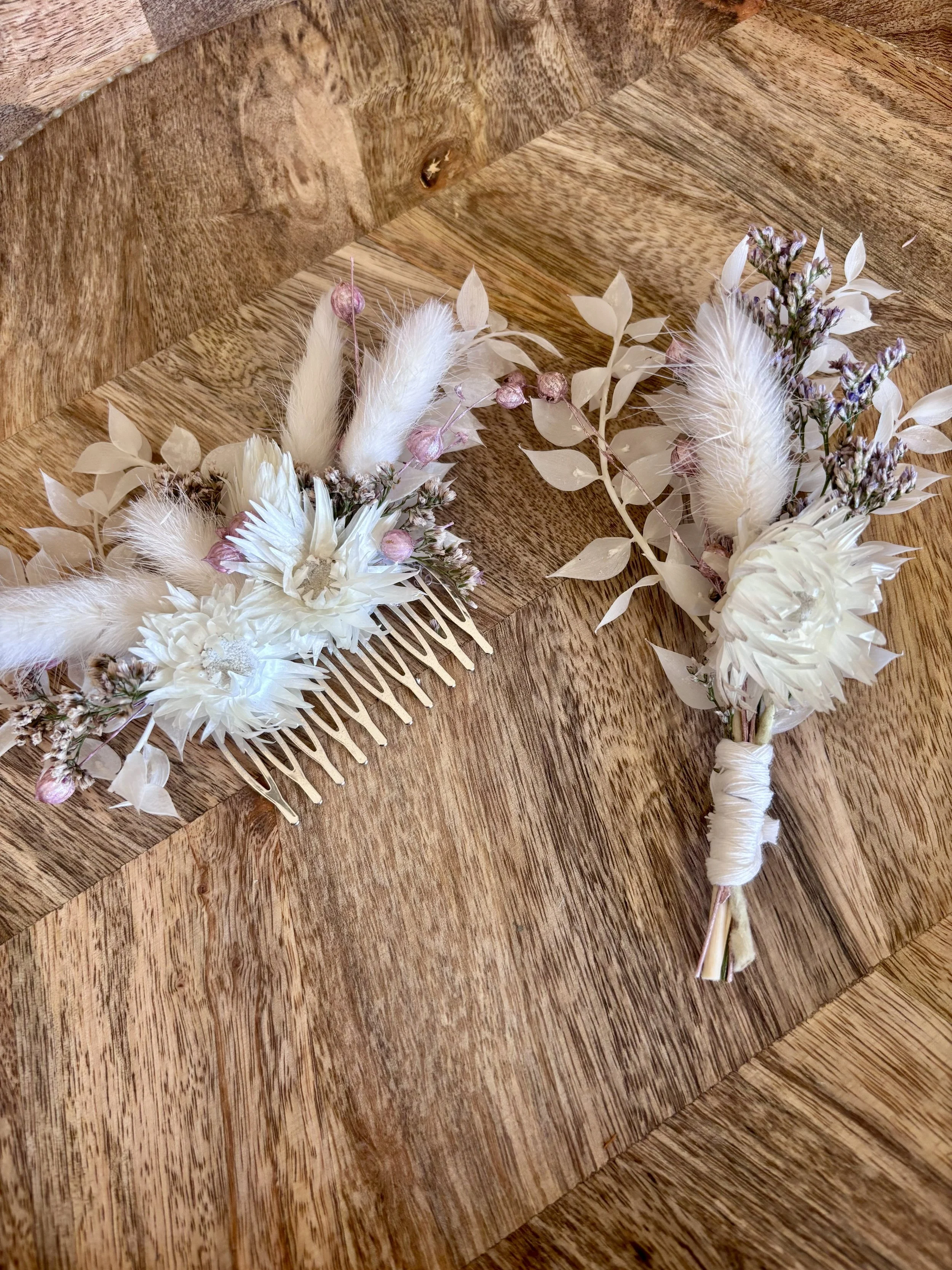 Deux accessoires de coiffure avec des fleurs blanches et des plantes séchées, posés sur une table en bois.