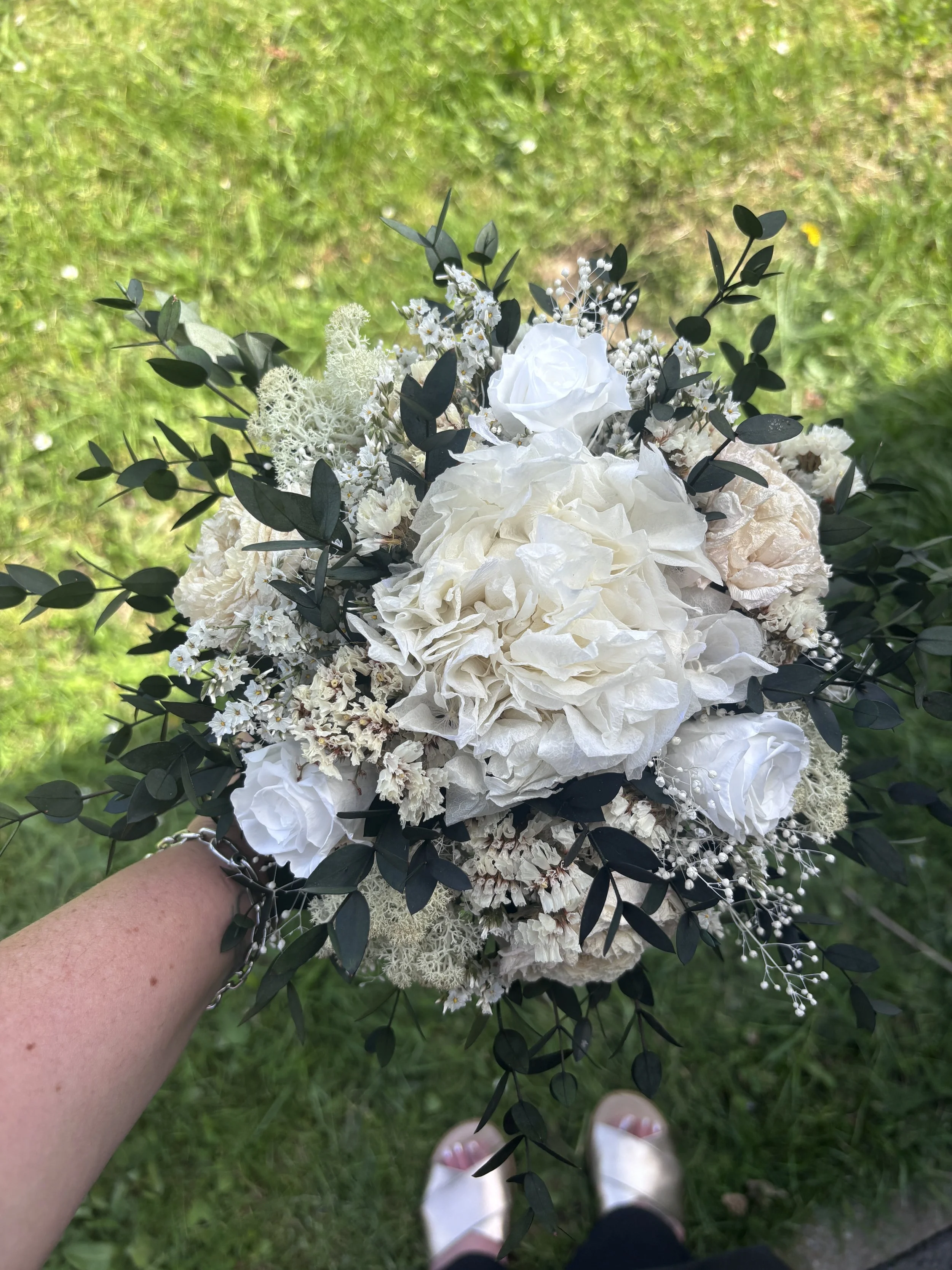 Bouquet de mariée bohème chic en fleurs séchées et stabilisées, composé de pivoines blanches, roses stabilisées, statice blanc, mousse végétale et feuillage d’eucalyptus noir. Cette création artisanale associe élégance, douceur et caractère pour un m