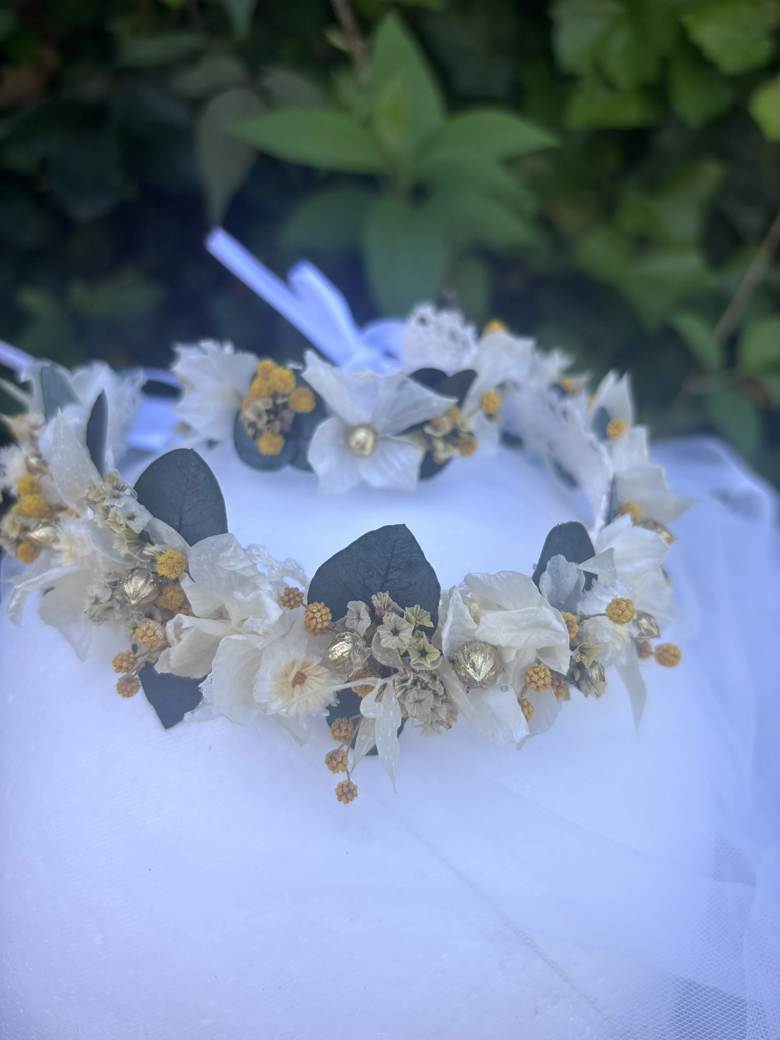 Une couronne de fleurs blanches avec des boutons dorés et des feuilles vertes, posée sur une surface blanche.