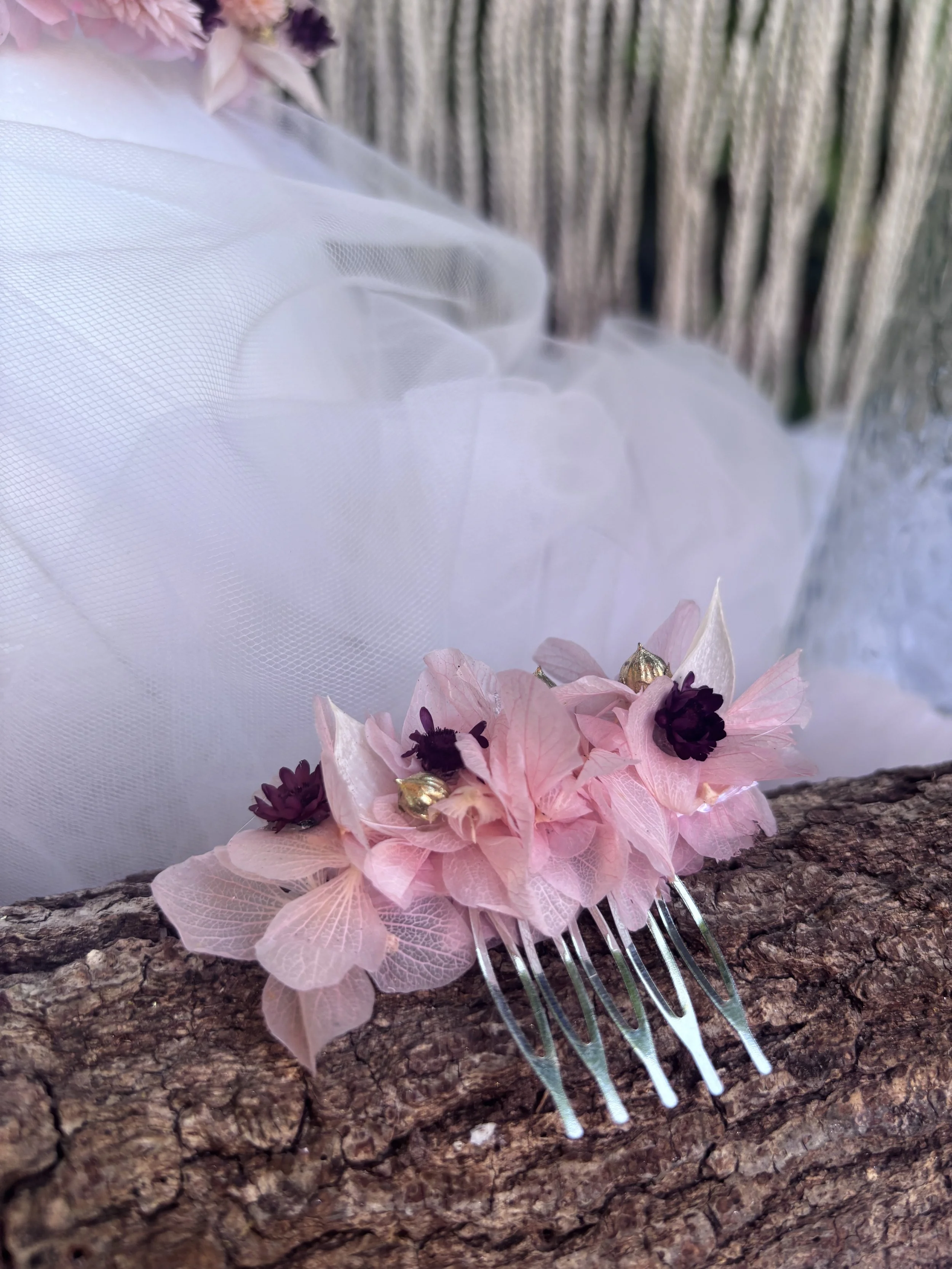 Une décoration florale composée de fleurs roses, violettes et or avec une barrette en métal, posée sur une surface en bois.